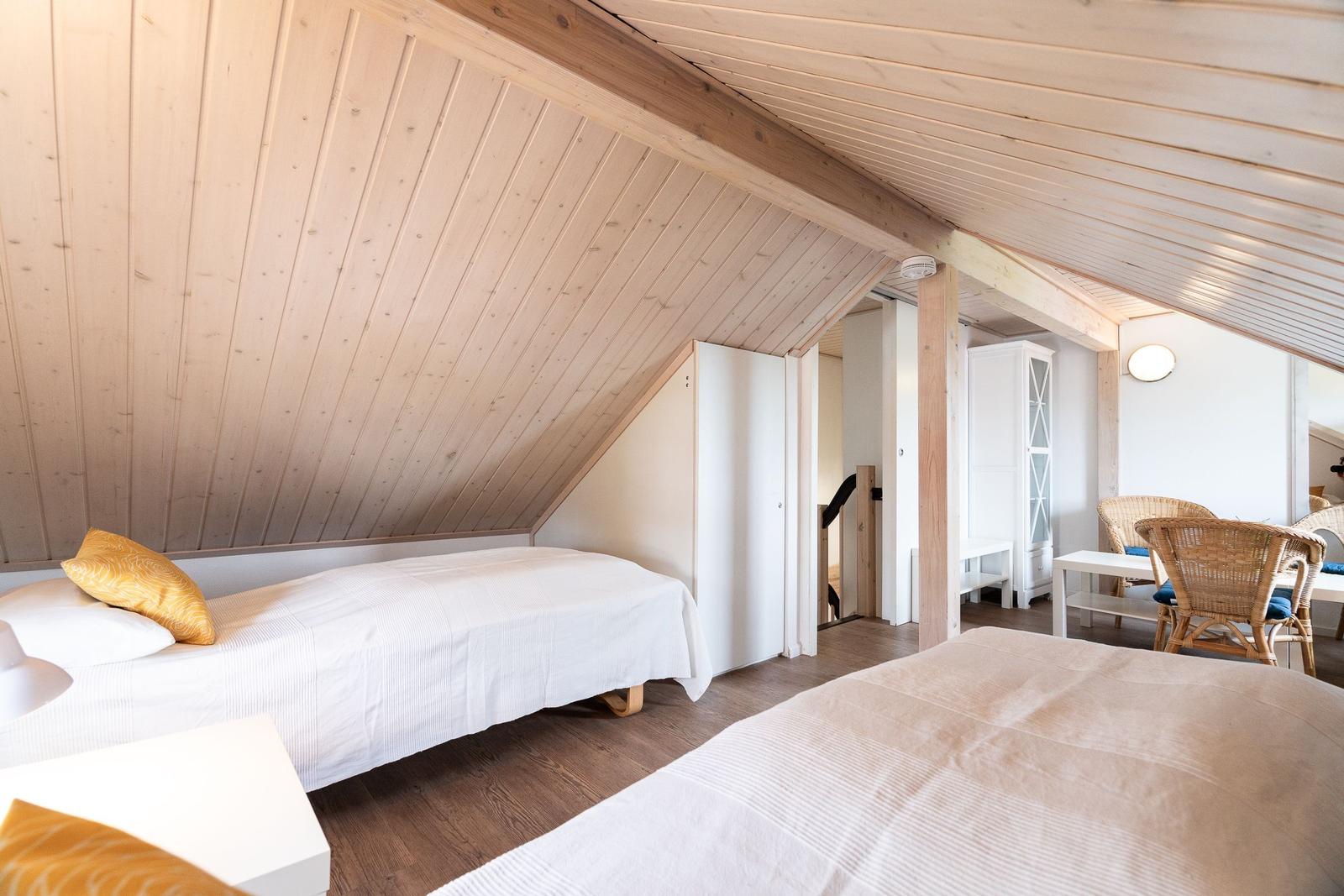 Room with two beds, wooden ceiling, and seating area in the background.