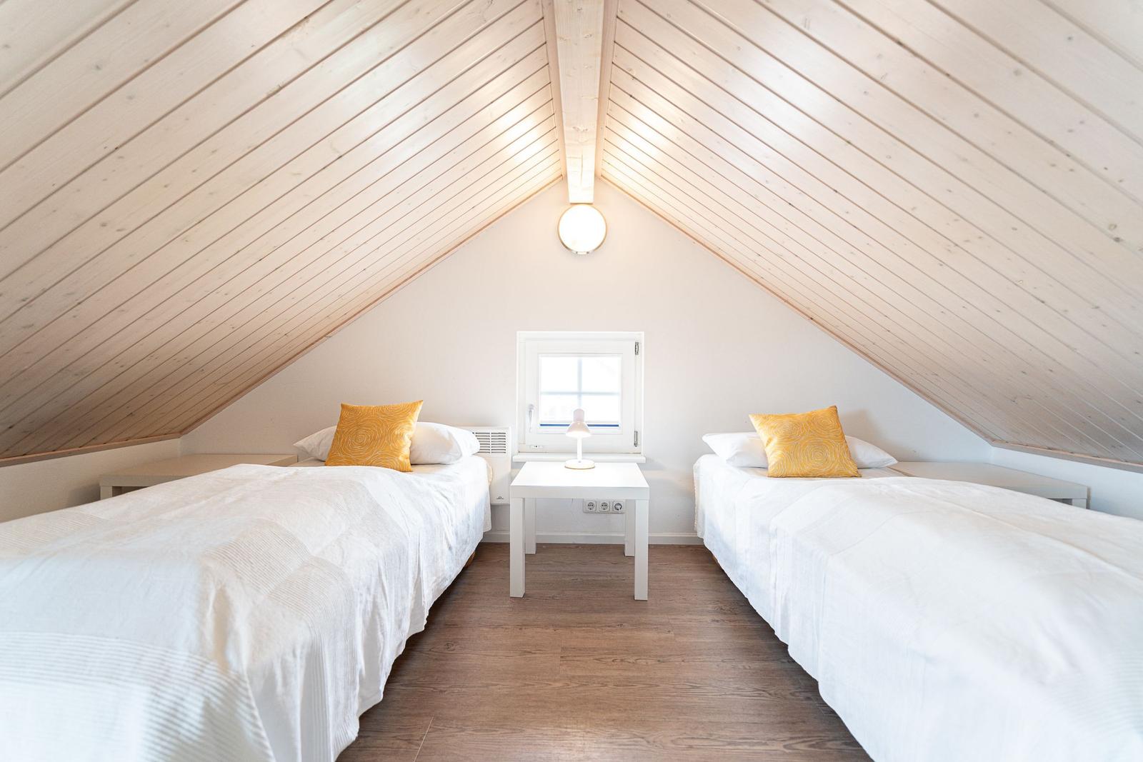 Two beds with white bedding and yellow pillows under a wooden ceiling