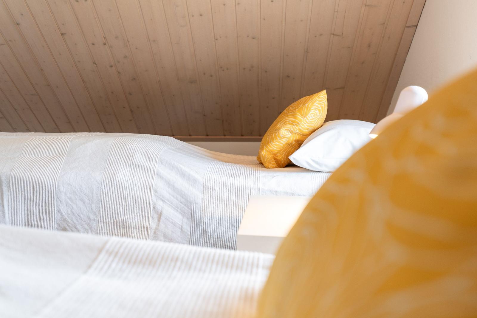 A bed with white bedding and yellow pillows under a wooden ceiling.