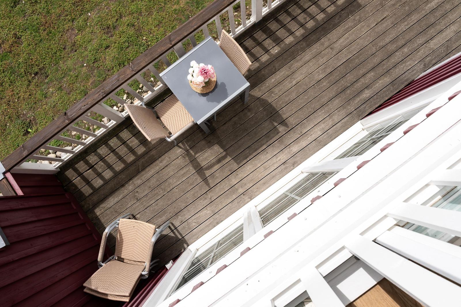 Deck with table, chairs, and floral arrangement. Wooden flooring and white railings.