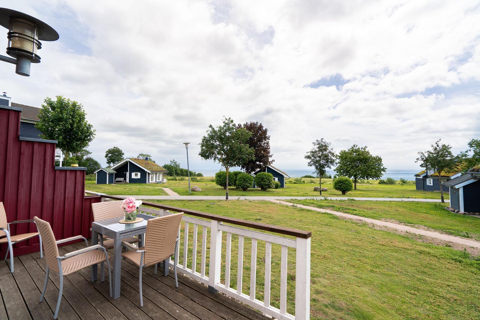 Deck with table and chairs, view of lawn and sea.