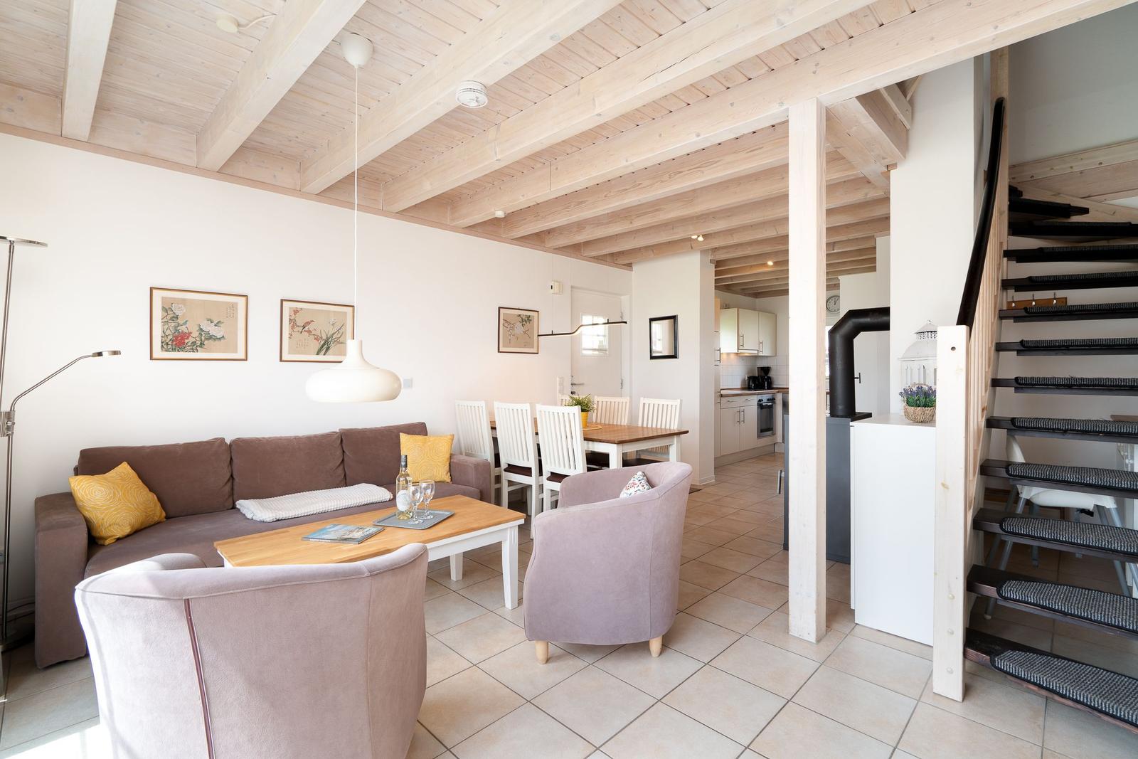 Living and dining area with wooden ceiling, sofa, chairs, and staircase.
