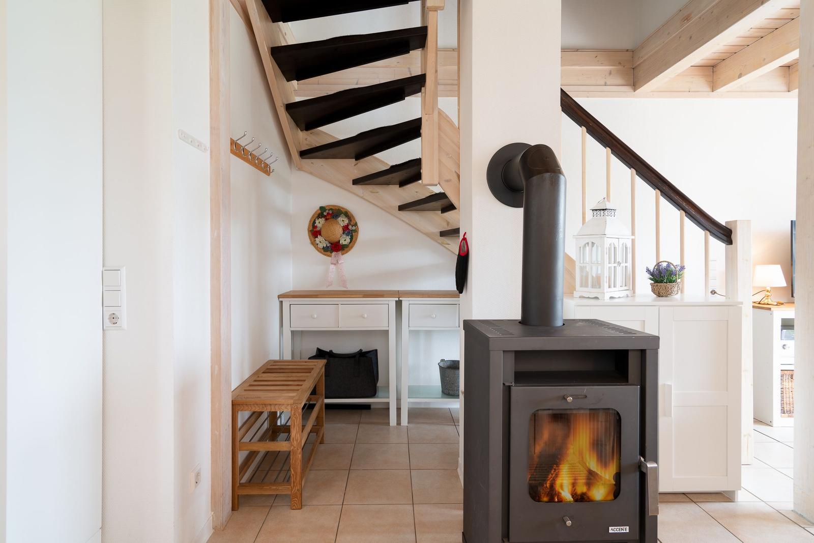 Entrance area with wood stove, staircase, and shoe cabinet. Tile floor and light walls.