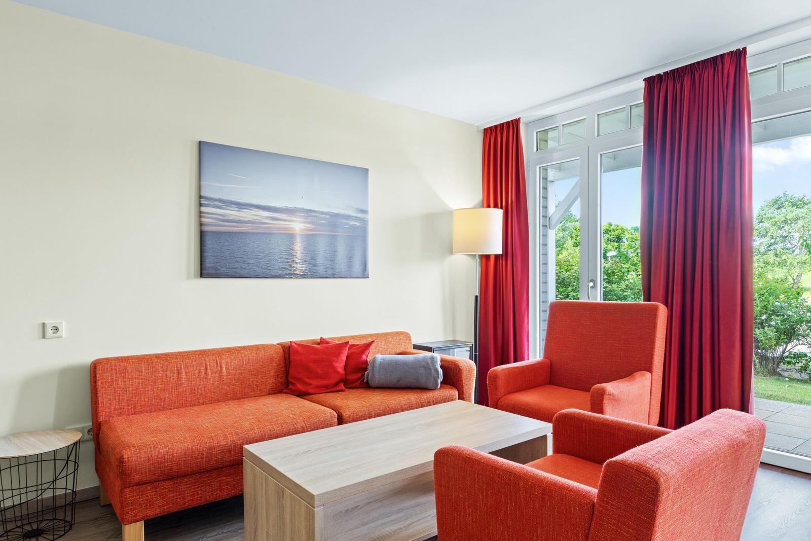 Ein Wohnzimmer mit orangefarbenen Sitzmöbeln, einem Tisch und einem Fenster mit roten Vorhängen.