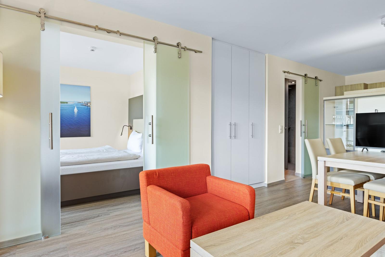 Wohnbereich mit Schlafzimmer, orange Sessel und Essbereich.
