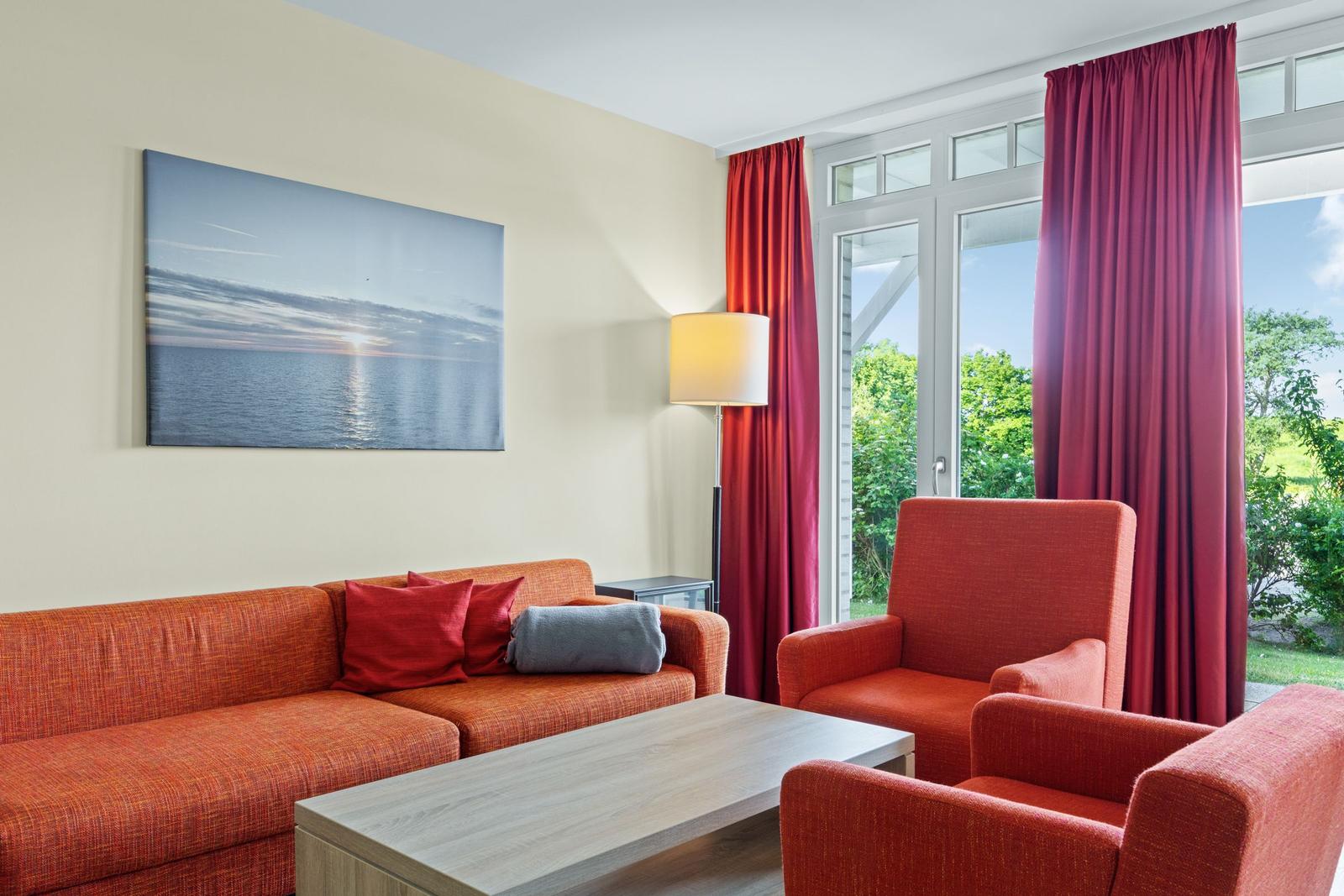 Ein Wohnzimmer mit rotem Sofa, zwei Sesseln und einem Fenster mit roten Vorhängen.