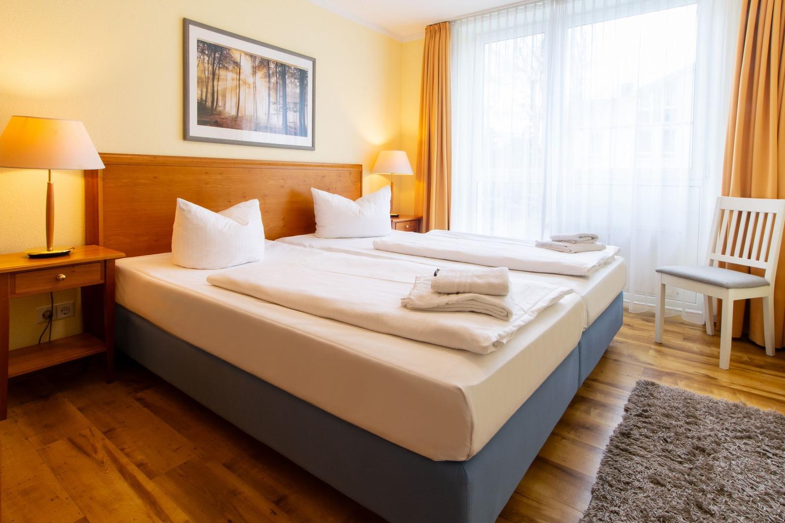 Ein Schlafzimmer mit Doppelbett, zwei Nachttischen, einem Stuhl und einem großen Fenster.