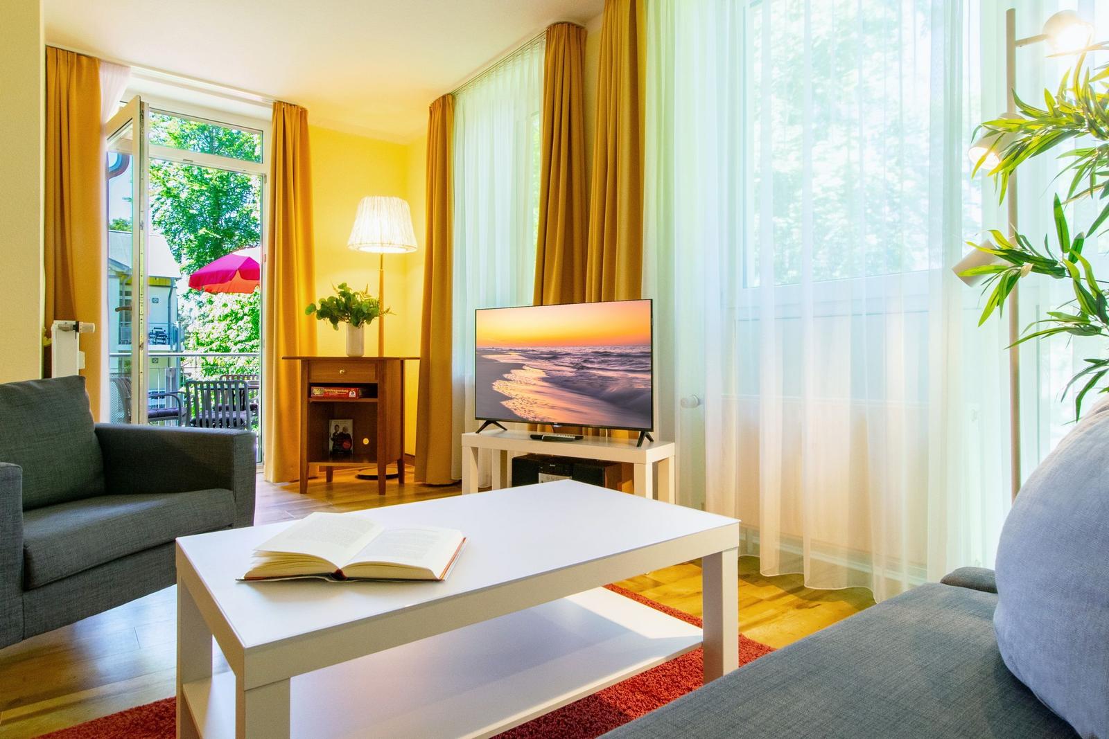 Wohnzimmer mit Sofa, Fernseher und Blick auf Balkon