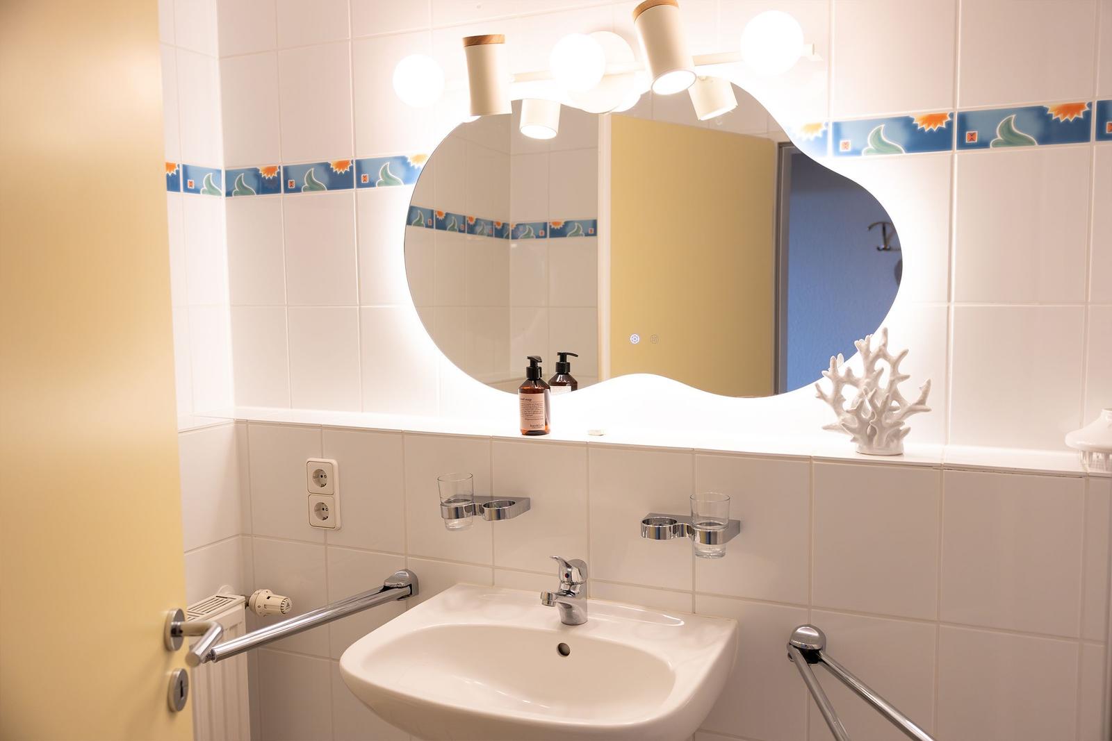 Badezimmer mit Waschbecken, Spiegel und Handtuchhalter. Wandfliesen mit dekorativer Bordüre.