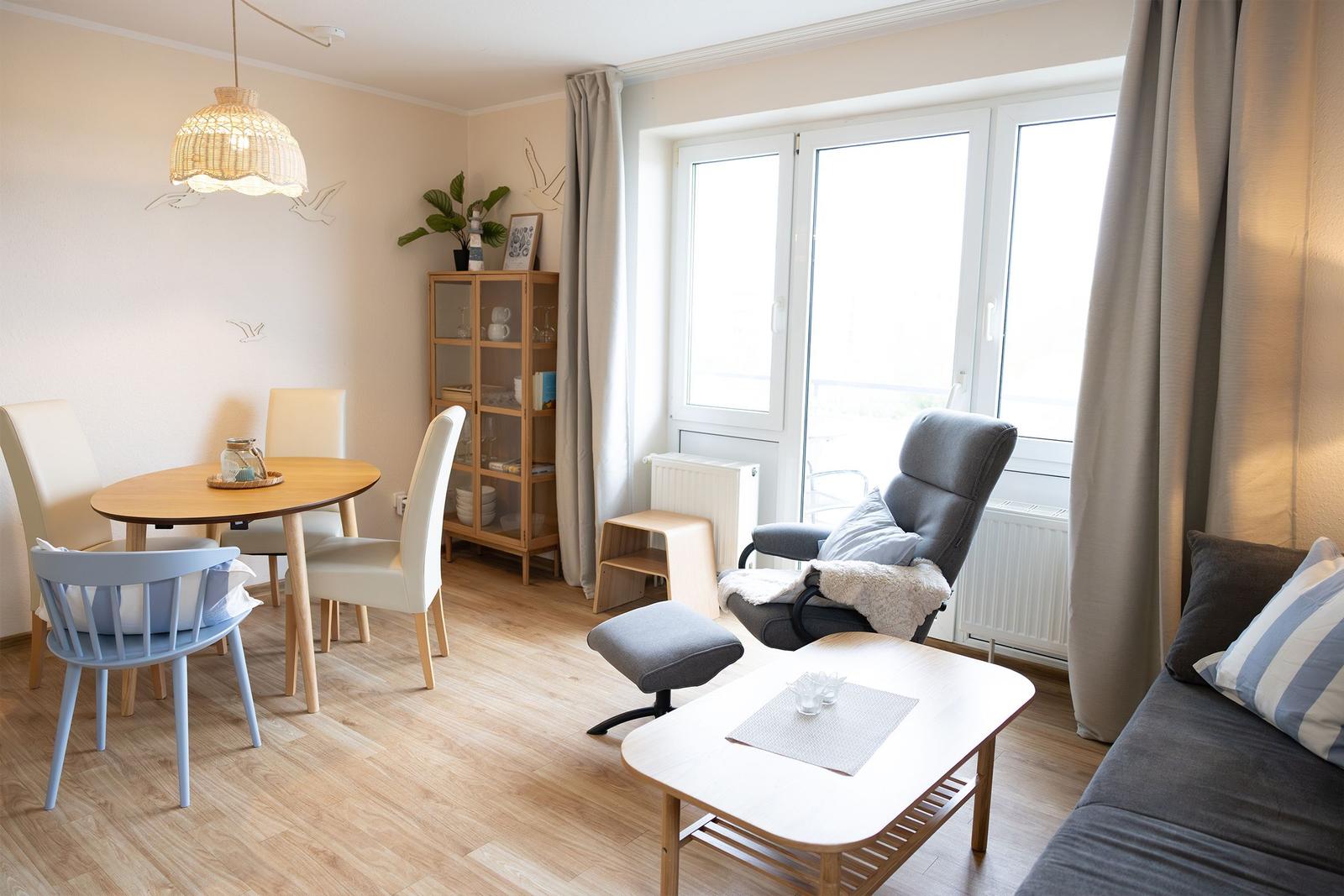 Wohn- und Essbereich mit Tisch, Stühlen, Sofa und Sessel. Große Fenster und Holzboden.