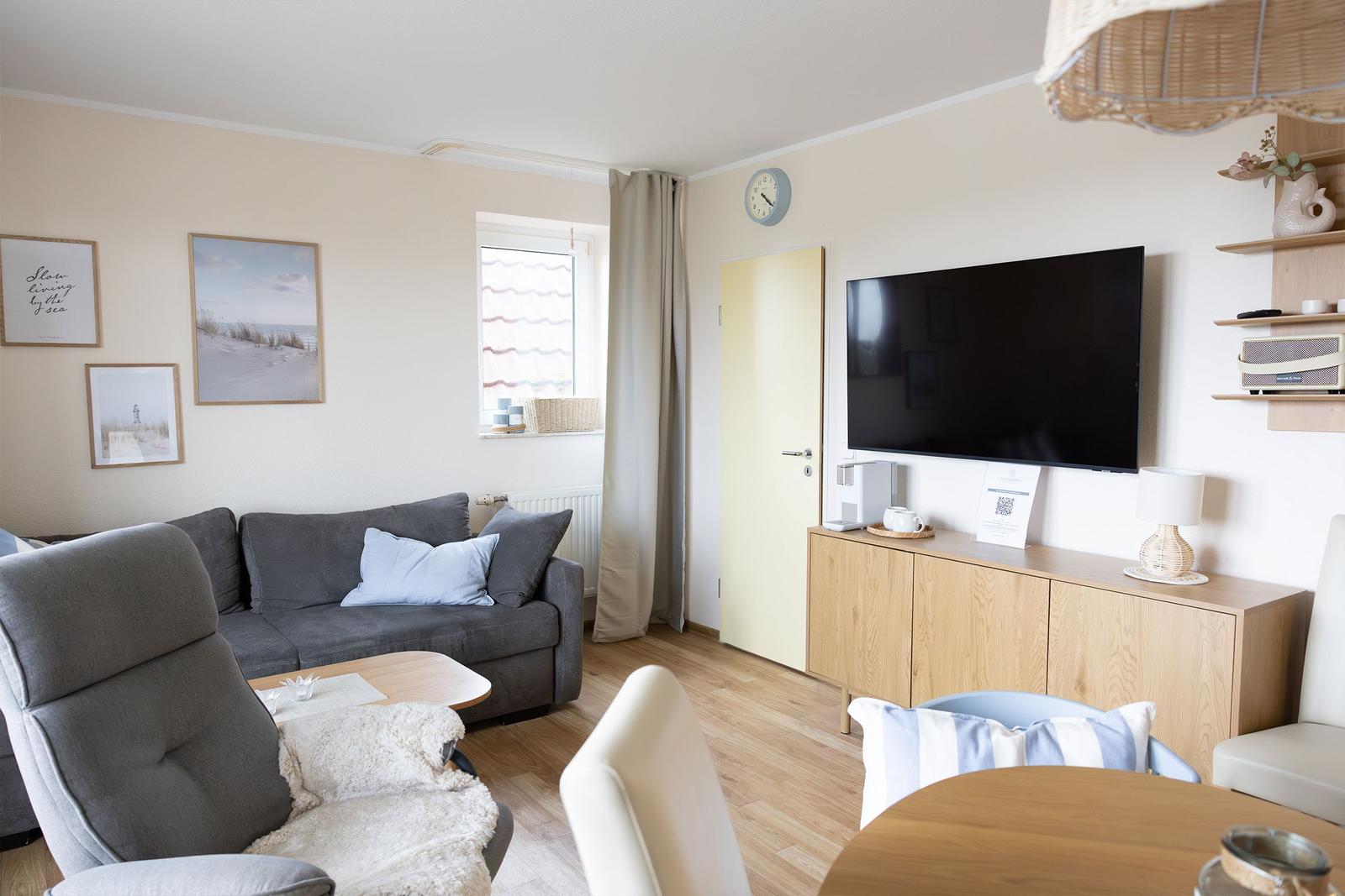 Wohnzimmer mit Sofa, Fernseher und Holzmöbeln. Fenster mit Vorhang und Wandbilder.