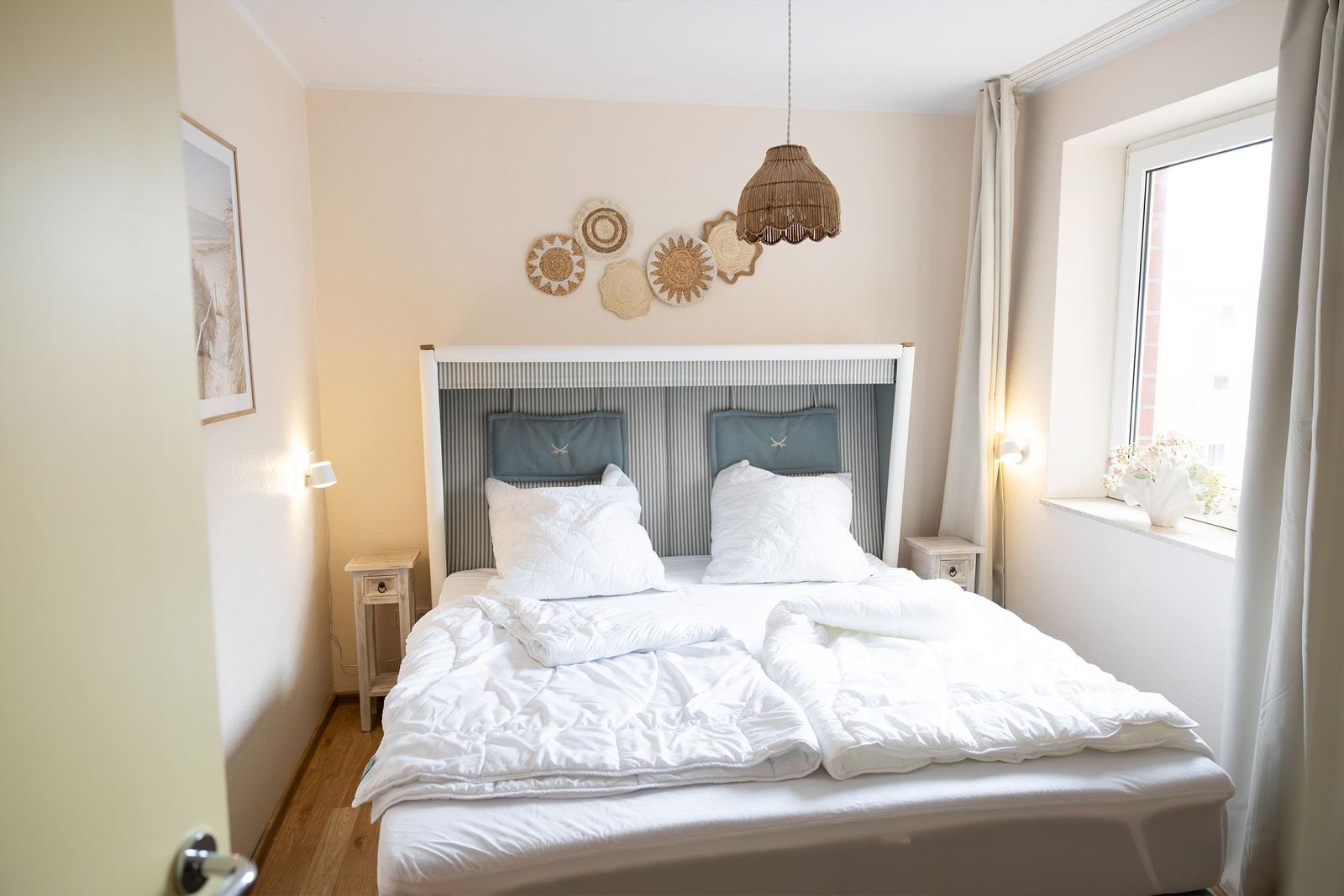 Schlafzimmer mit Doppelbett, Wanddekoration und Fenster mit Vorhängen.
