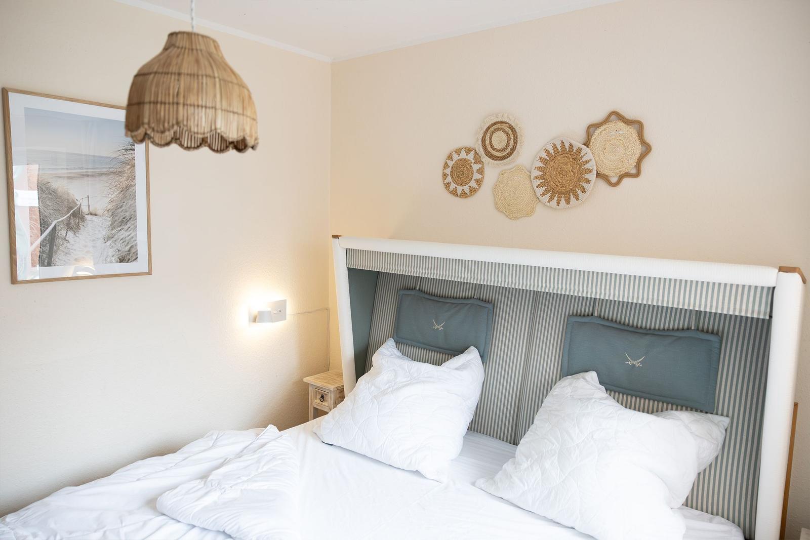 Schlafzimmer mit Bett, Wanddekoration und Pendelleuchte.