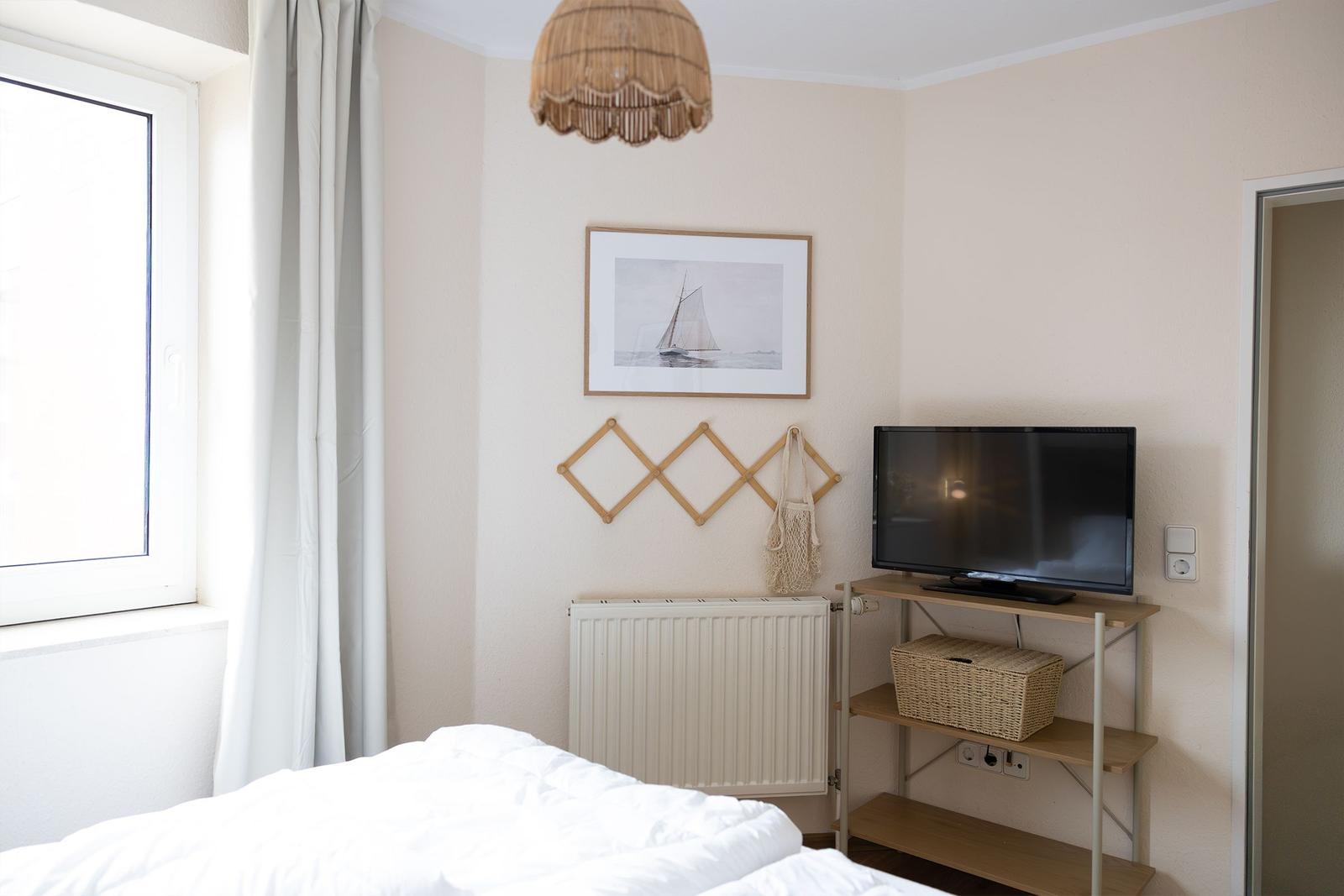 Schlafzimmer mit Bett, Fernseher und Wandbild. Fenster mit Vorhängen.