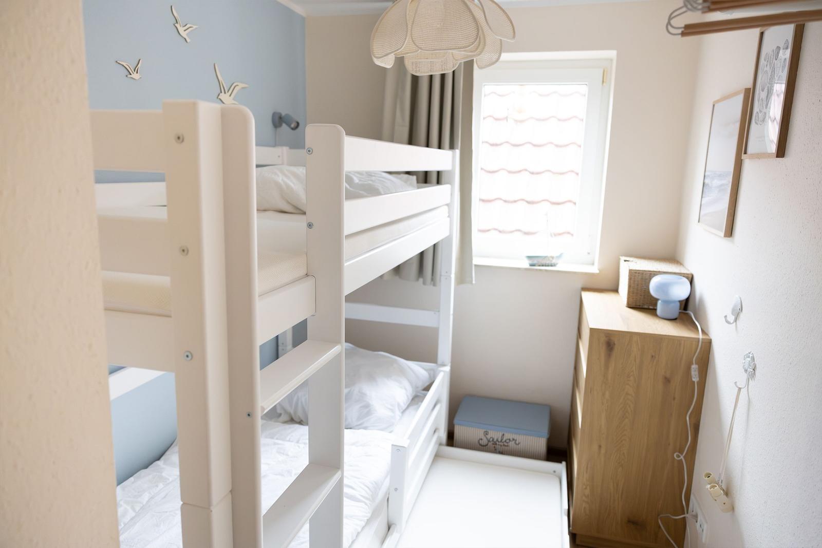 Ein Schlafzimmer mit einem weißen Doppelstockbett, einem Fenster und einem Holzschrank.