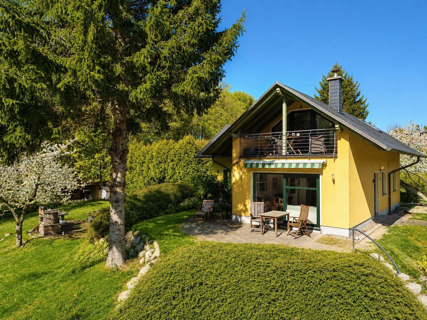 A yellow house with a balcony, garden, and wooden furniture under a blue sky.