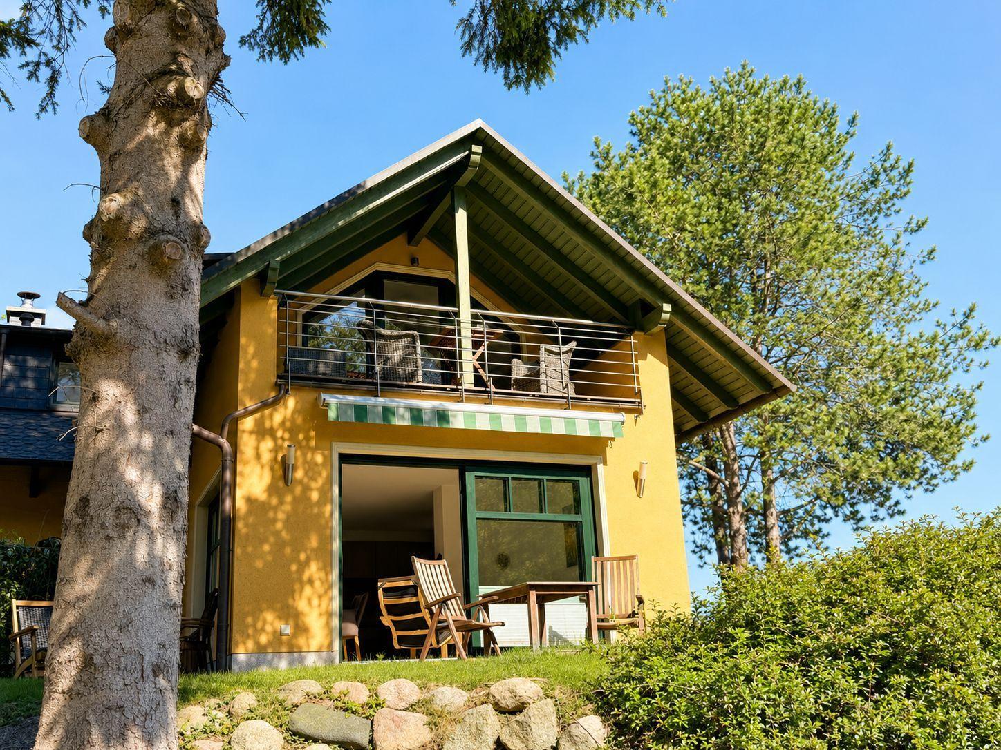 A yellow house with balcony and terrace under trees.