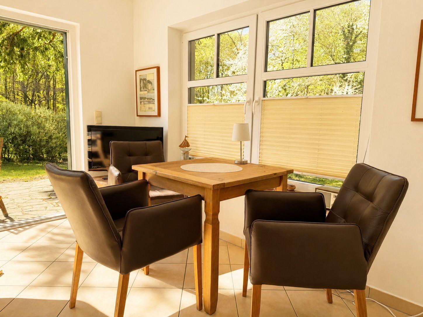 Dining area with wooden table and four brown chairs. Large windows and glass door to garden.