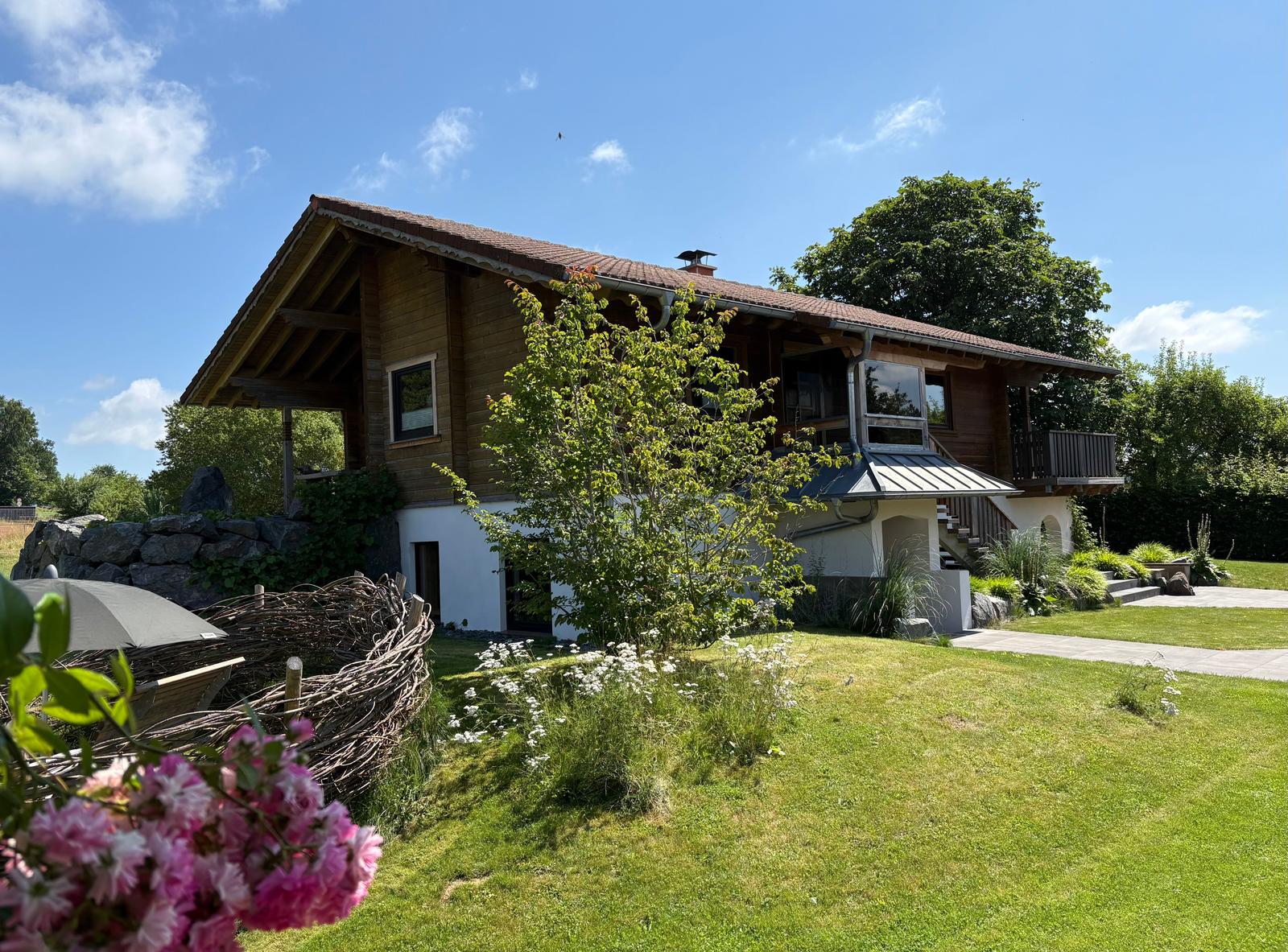 Holzhaus mit Balkon, Garten und blauem Himmel.