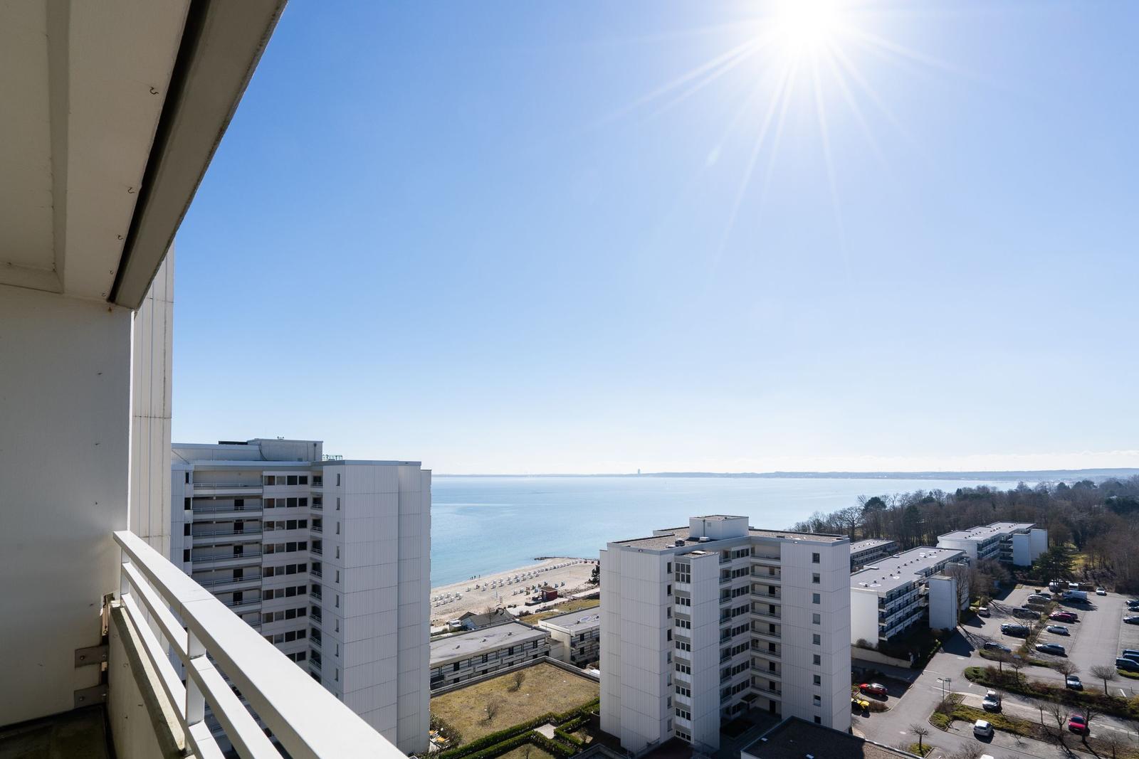 Blick vom Balkon auf das Meer und umliegende Gebäude unter strahlendem Sonnenschein.