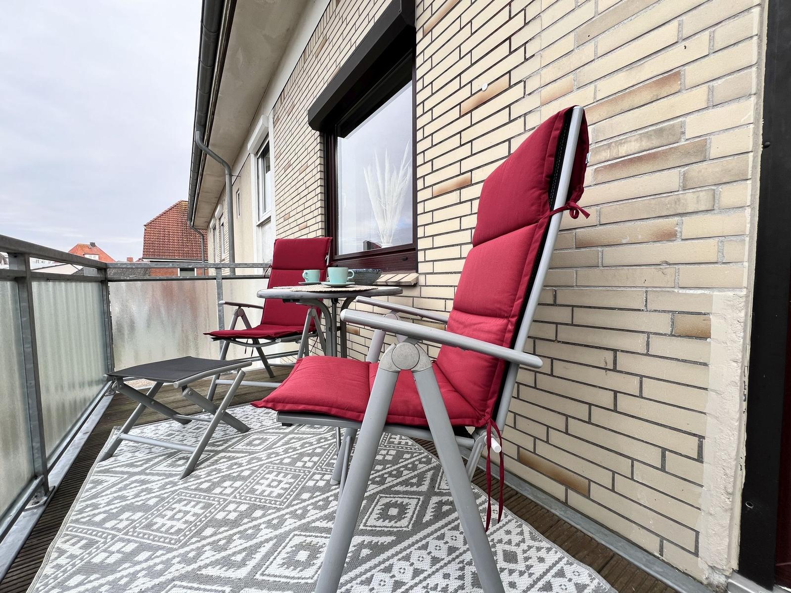 Terrasse mit zwei roten Liegestühlen, Tisch und Teppich vor Backsteinwand.
