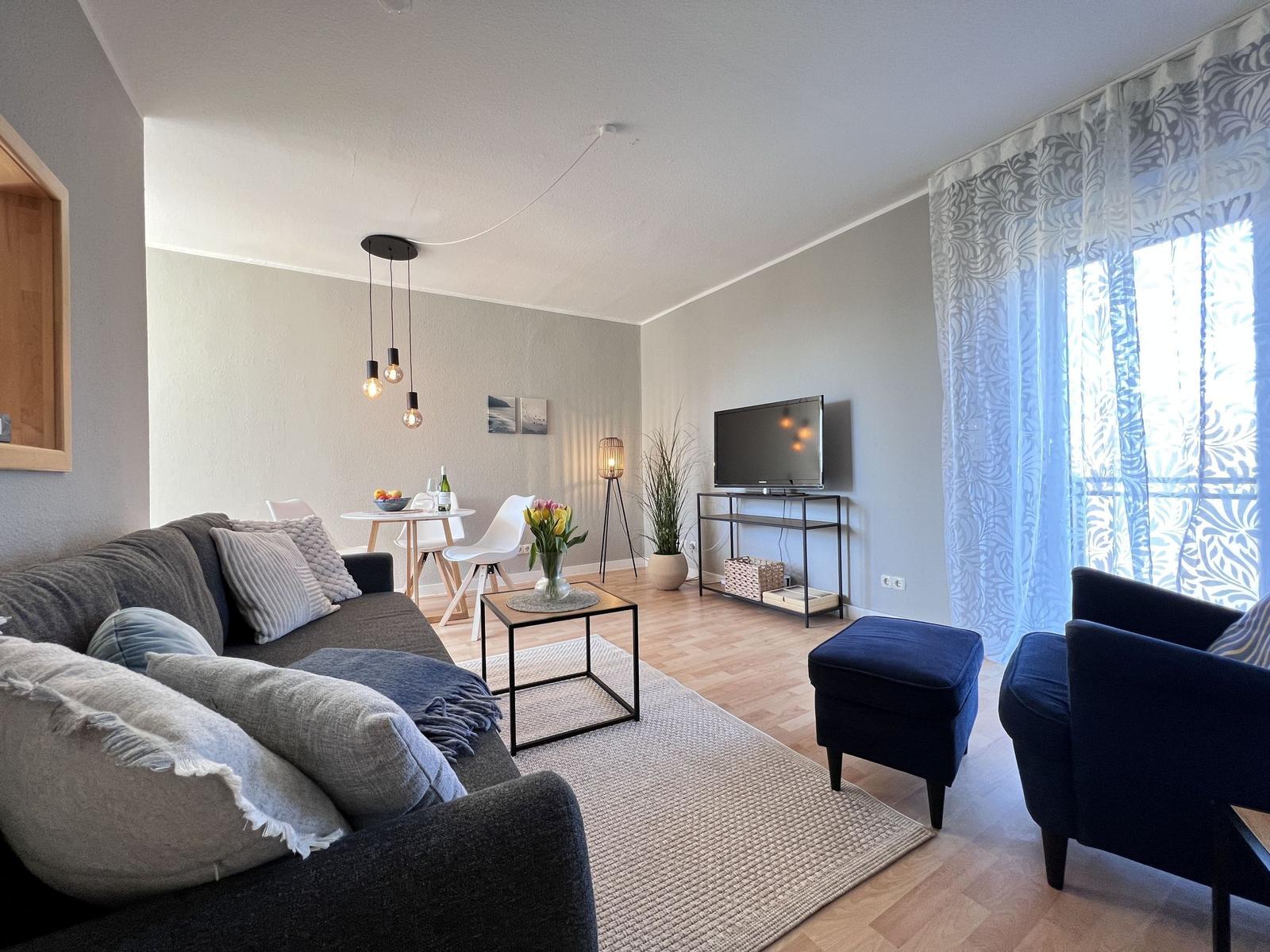 Wohnzimmer mit Sofa, Sessel, Fernseher und Esstisch.