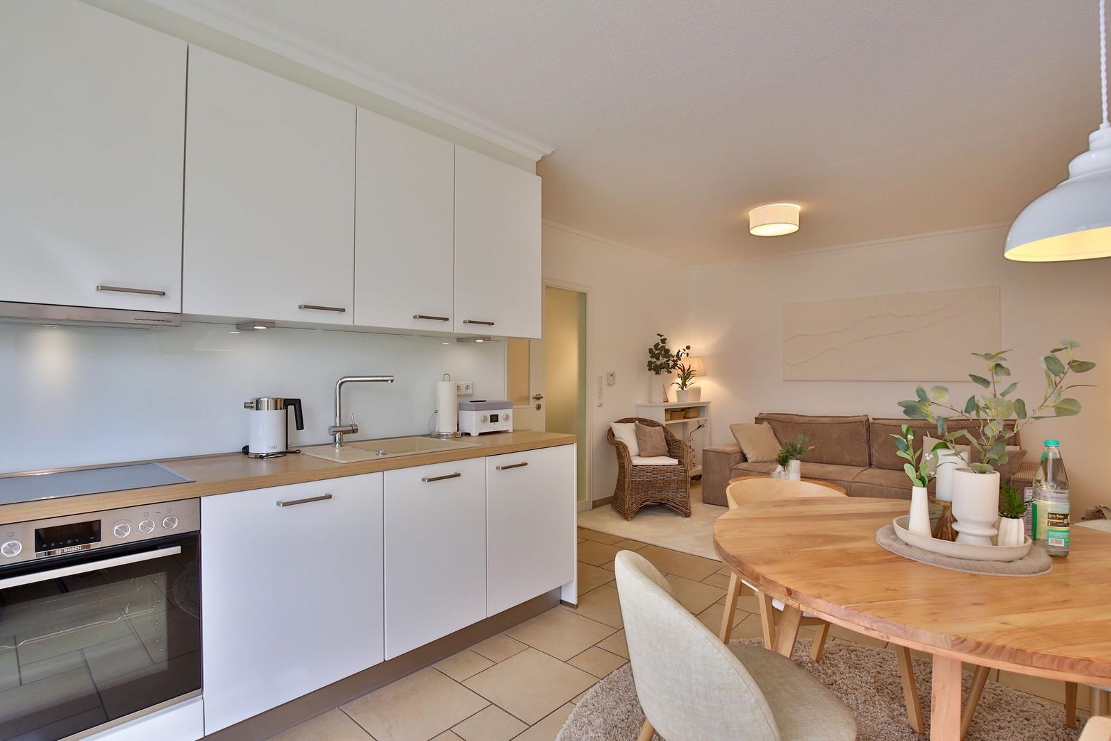 Kitchen with white cabinets and wooden countertop. Living area with sofa and dining table.