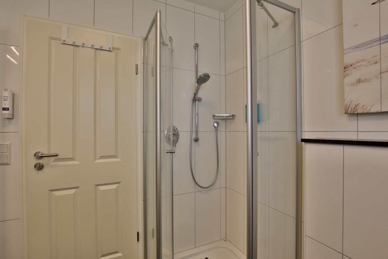 Shower cabin with glass door, shower head, and handheld shower. White tiles and door.