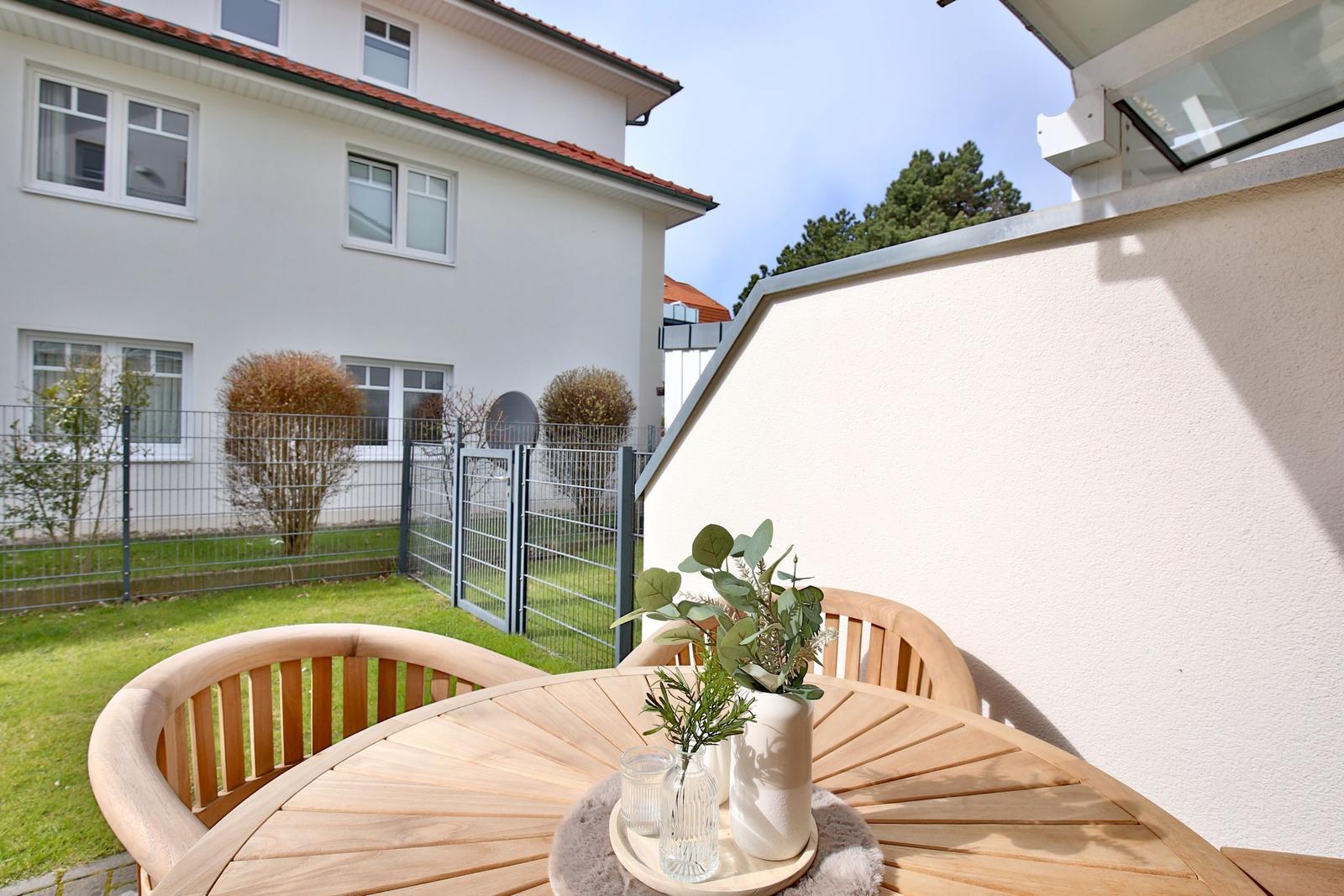 Terrace with wooden table and chairs, plants, and view of garden and neighboring house.