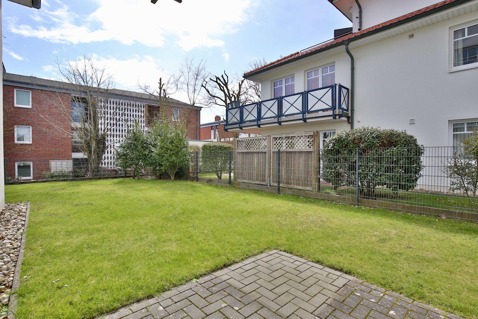 Rear yard with lawn, paved path, and balcony on the white facade.