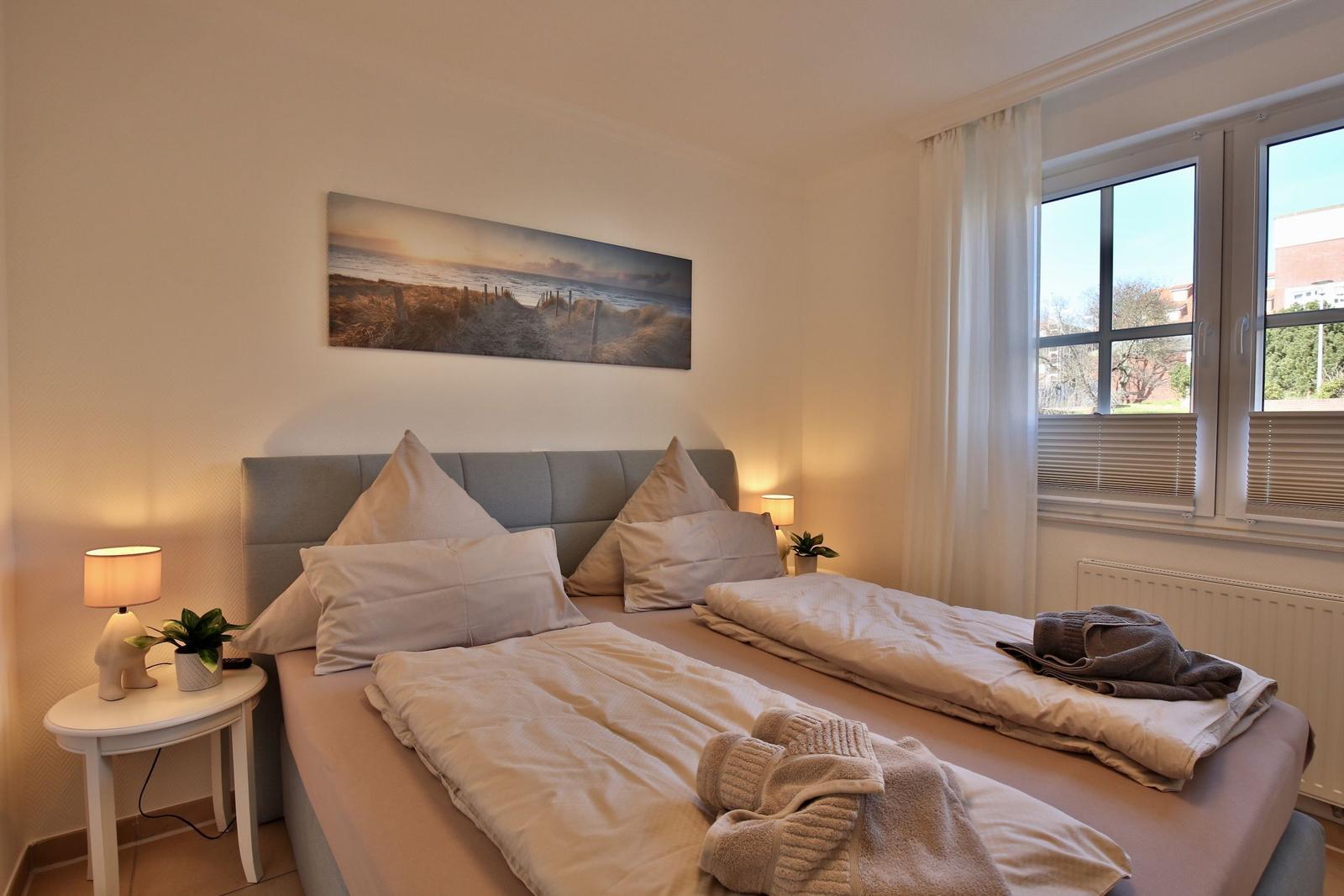 Bedroom with double bed, wall art, and window with view outside.