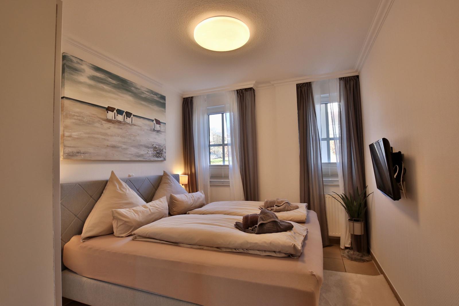 Bedroom with bed, windows, TV, and wall art.