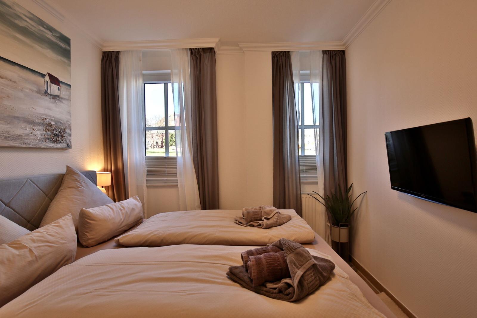 Room with double bed, two windows, TV, and wall art.