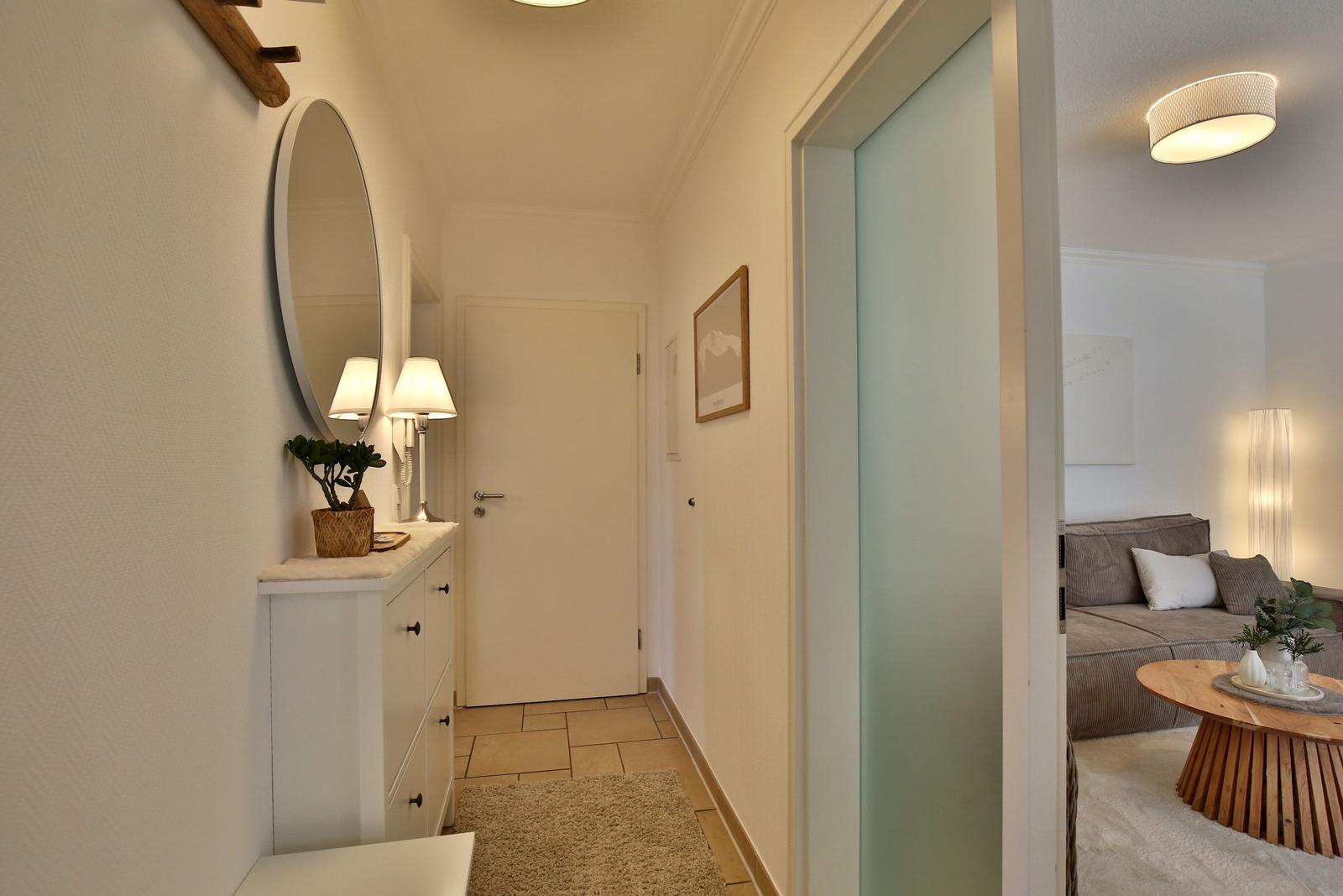 Hallway with mirror and cabinet. Entrance to living room with sofa and table.