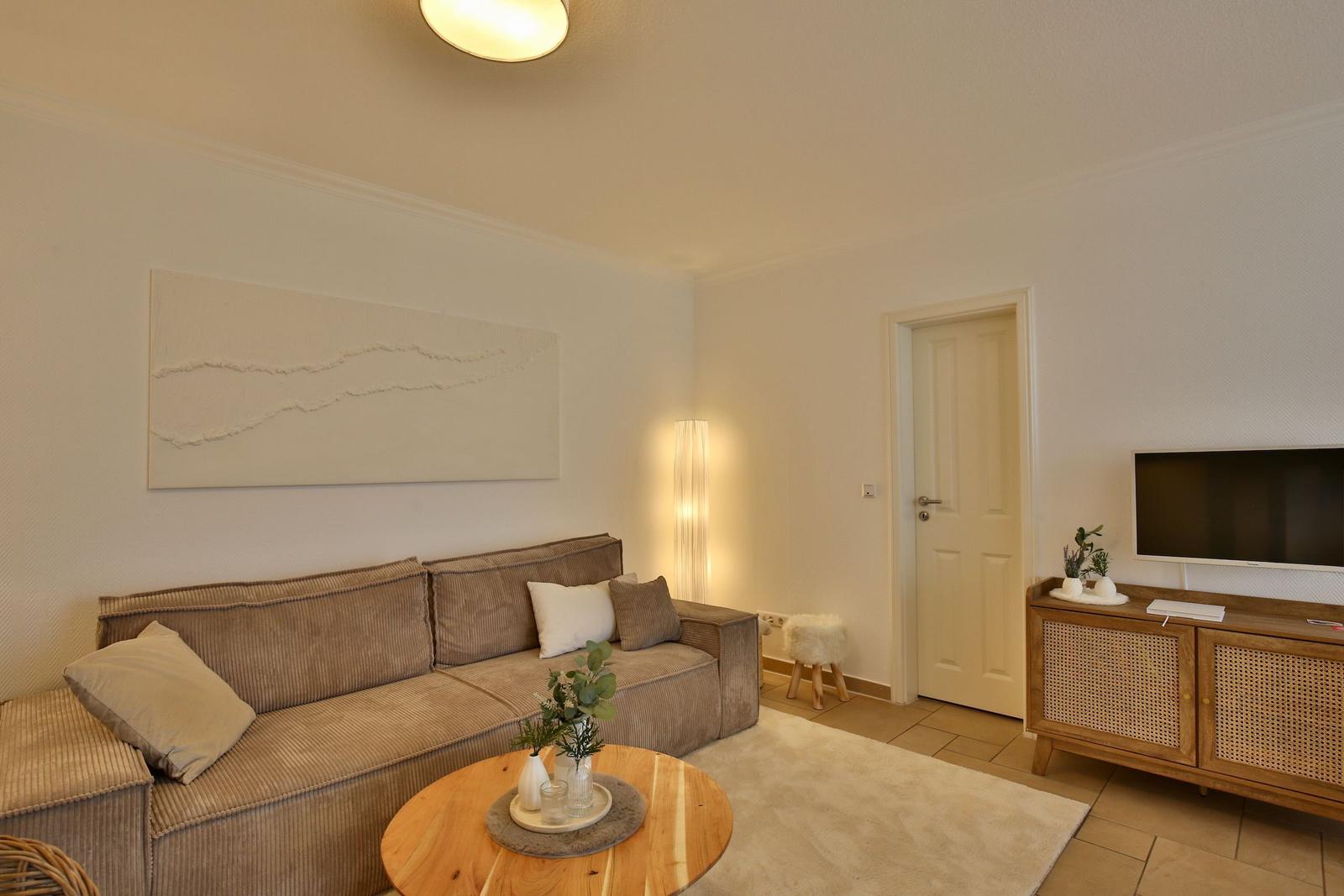 Living room with sofa, round table, and TV on wooden cabinet.