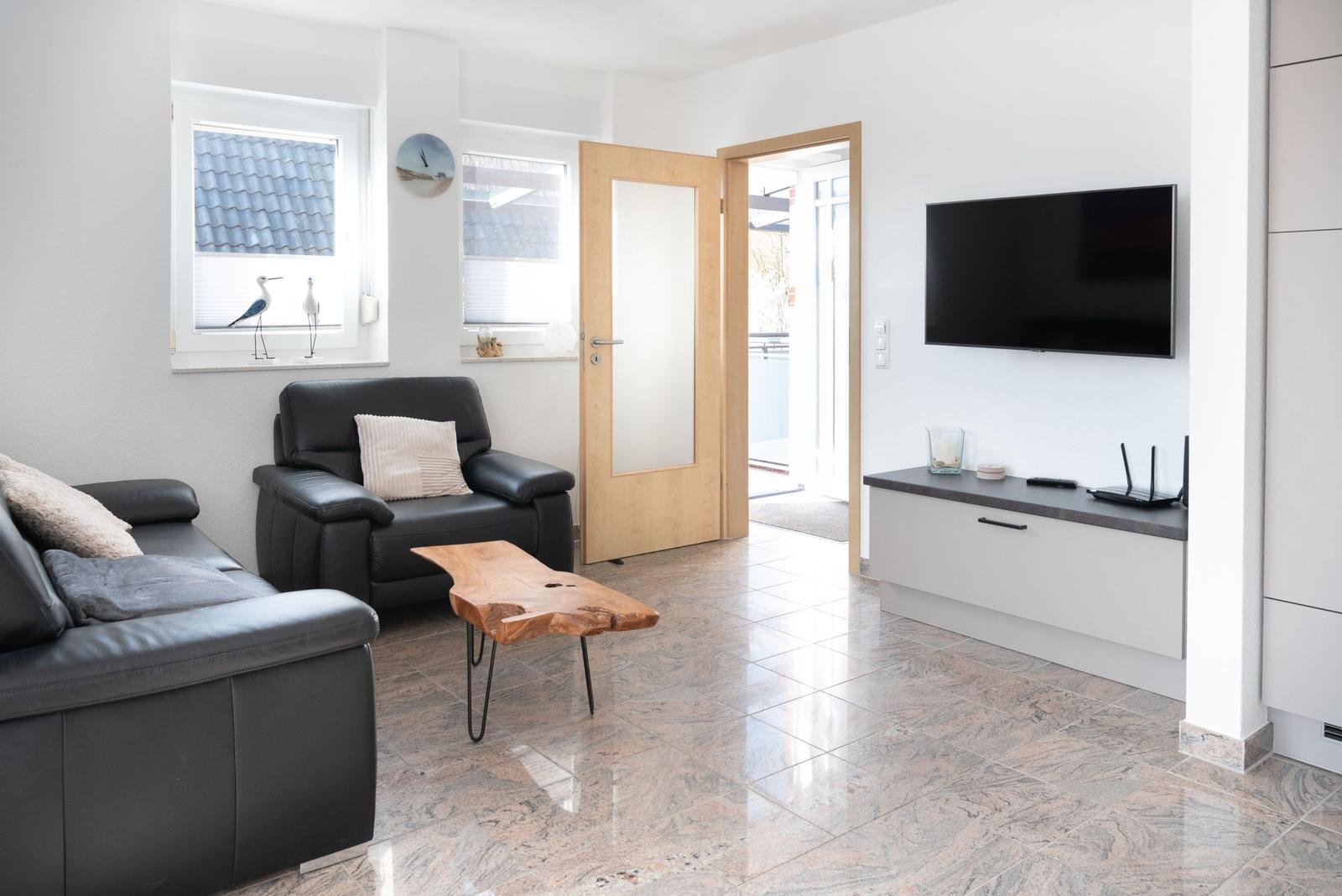 Wohnzimmer mit Ledersofa, Fernseher und Holztisch auf Marmorfliesen