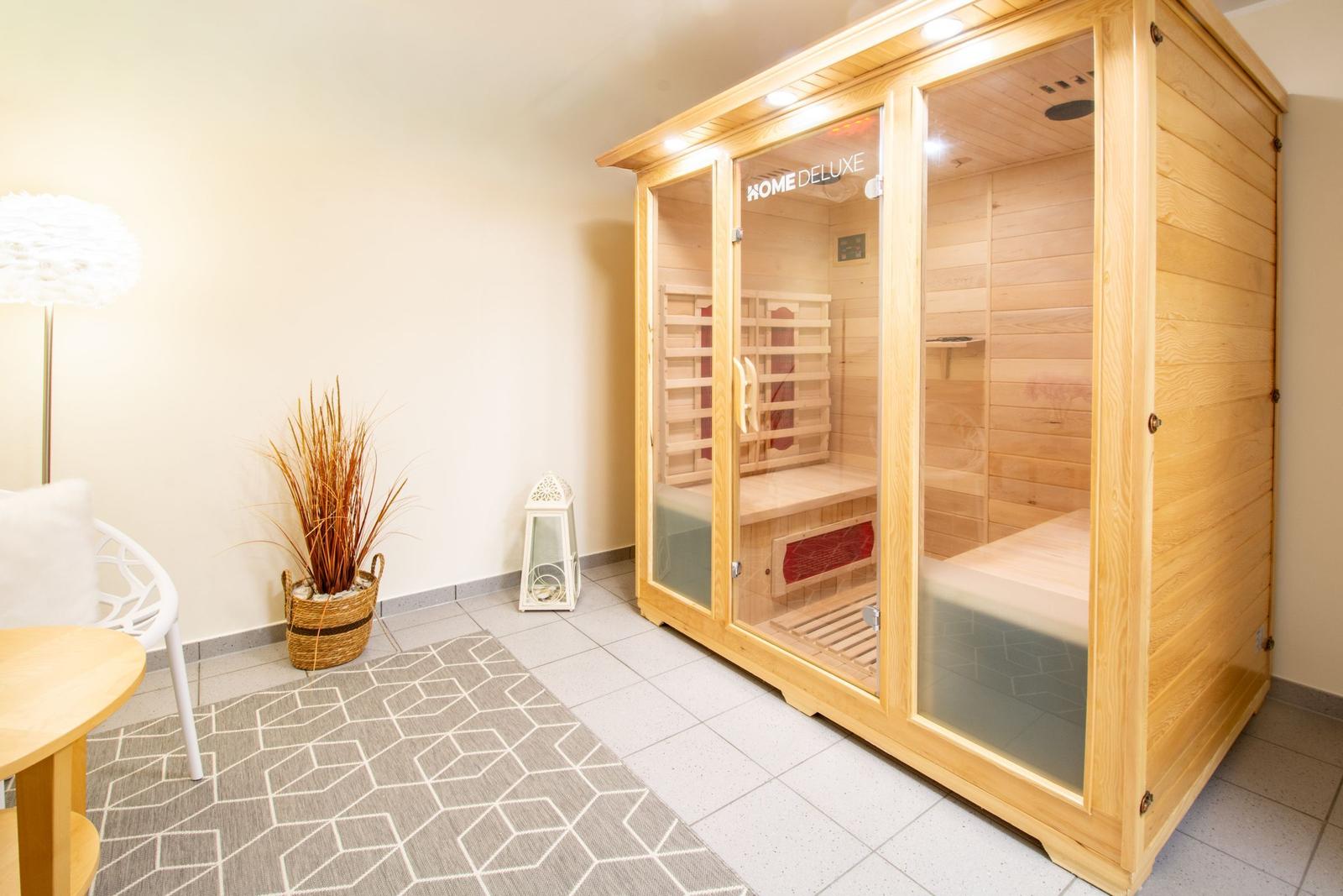 Holzsauna mit Sitzbänken und Glasfront. Nebenraum mit Stuhl, Tisch und Pflanze.