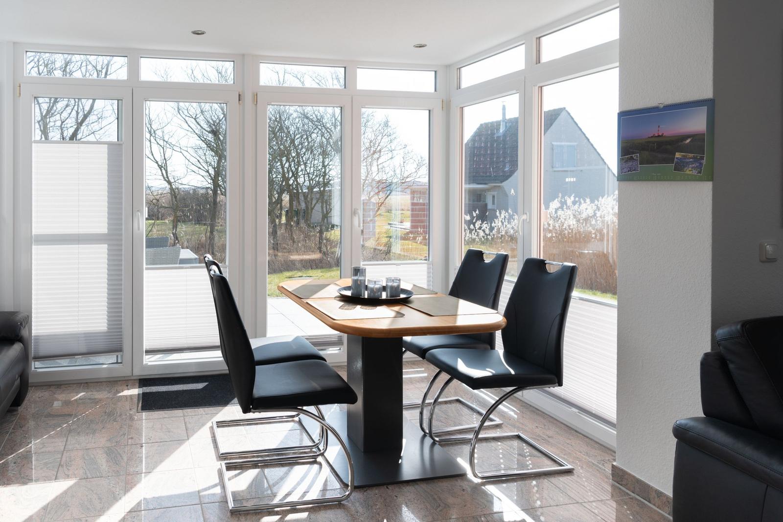 Esszimmer mit Tisch und Stühlen, große Fensterfront und Blick auf Garten.