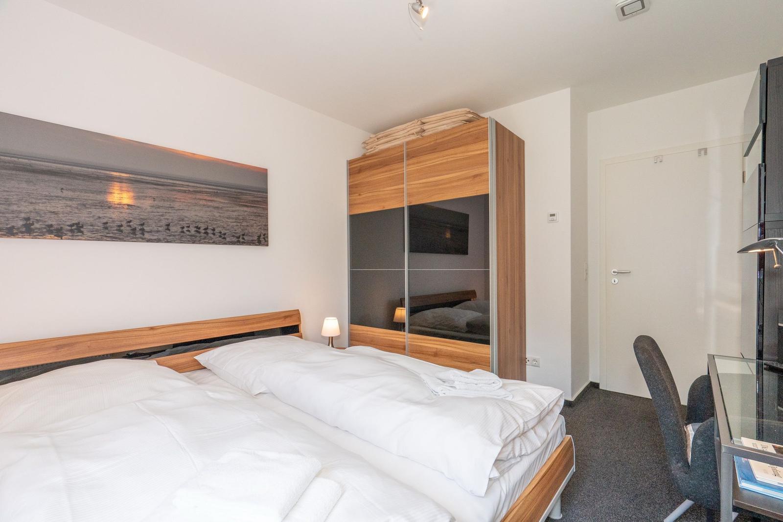 Schlafzimmer mit Bett, Kleiderschrank und Schreibtisch.