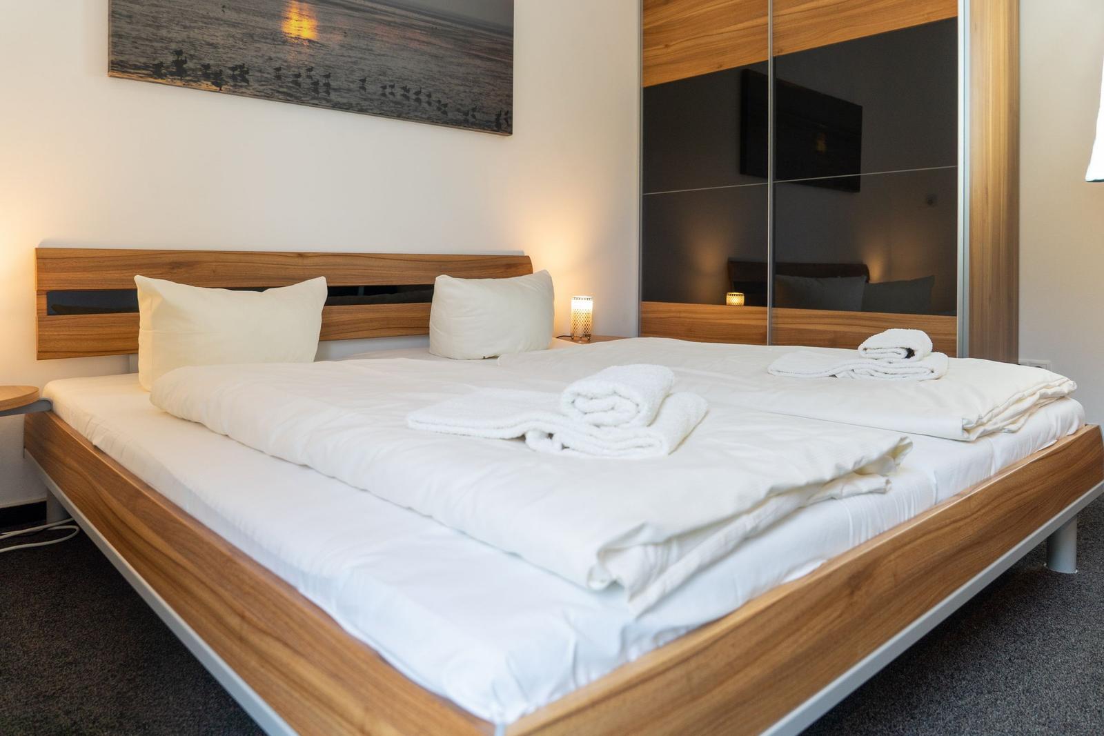Schlafzimmer mit Bett, Wandbild und Spiegelschrank.