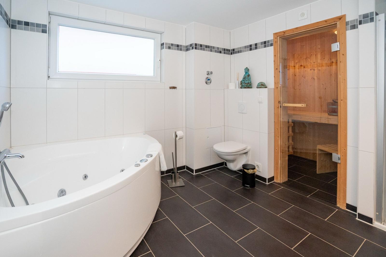 Bad mit Whirlpool, Toilette und Sauna im Hintergrund.