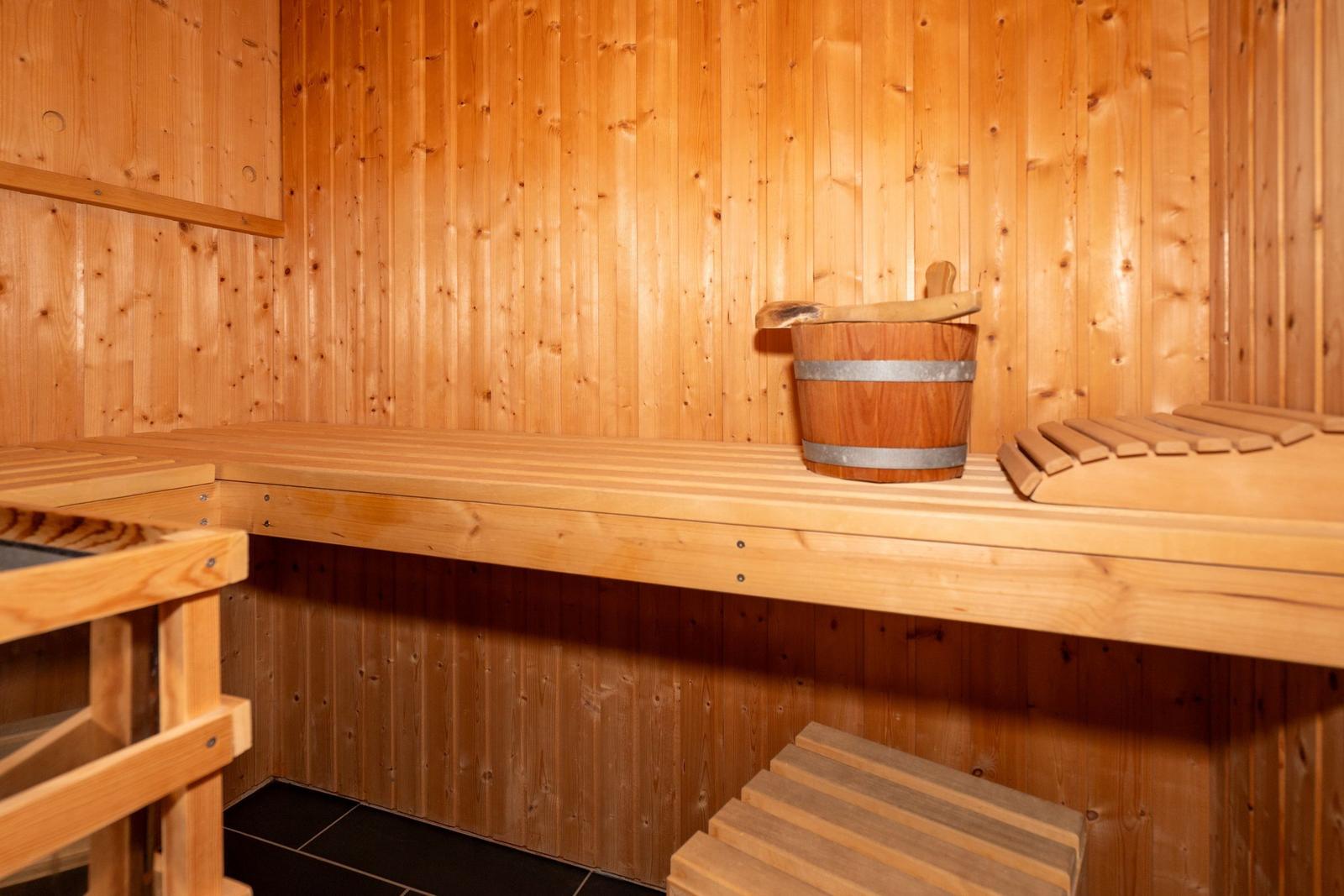 Sauna mit Holzbank, Eimer und Besen. Wände und Boden sind aus Holz.