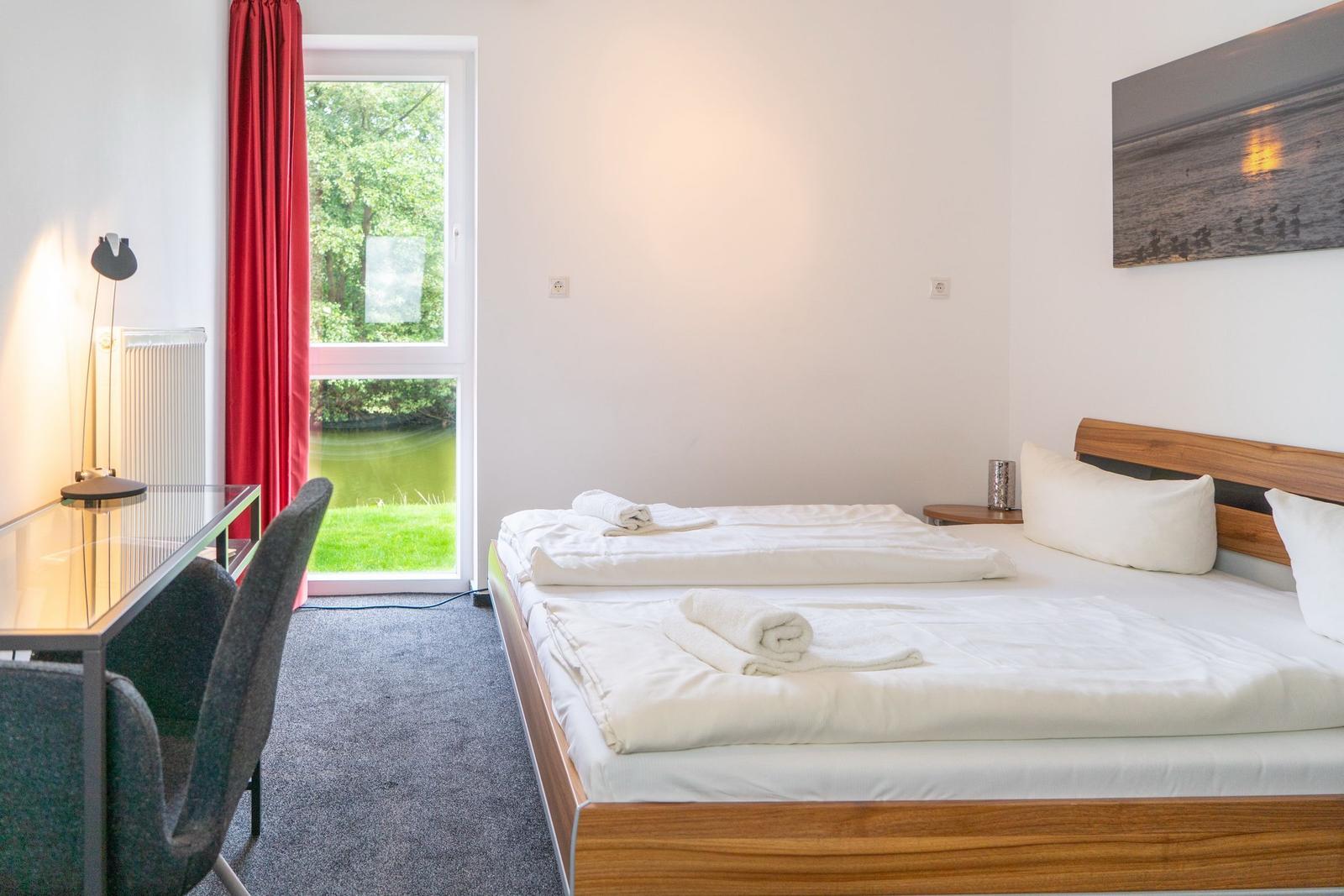 Schlafzimmer mit Doppelbett, Schreibtisch und Fensterblick auf einen See.