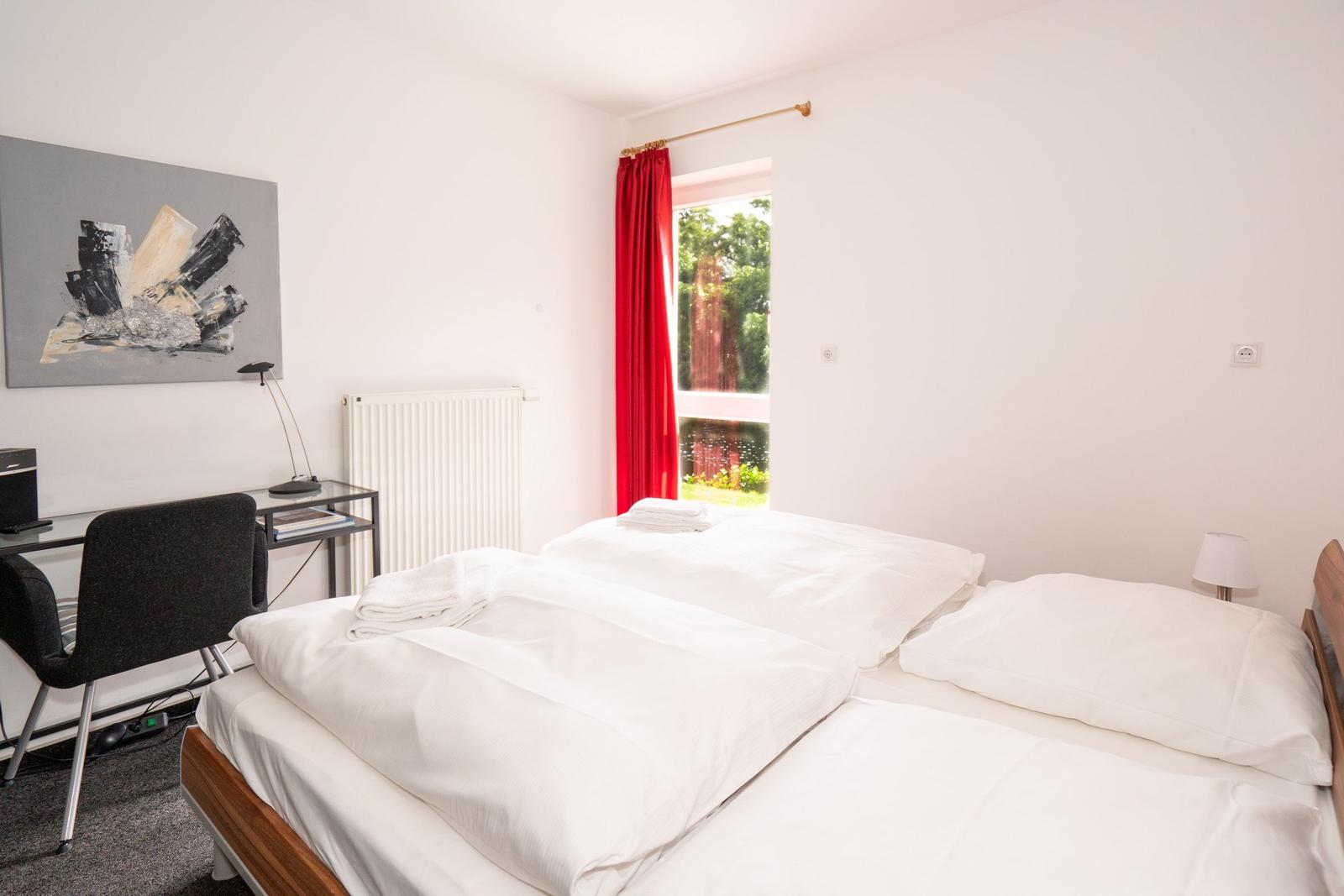 Schlafzimmer mit Bett, Schreibtisch und Fenster mit rotem Vorhang.