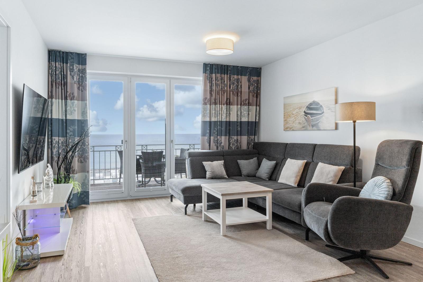 Wohnzimmer mit Sofa, Sessel und Blick auf den Balkon mit Meerblick.