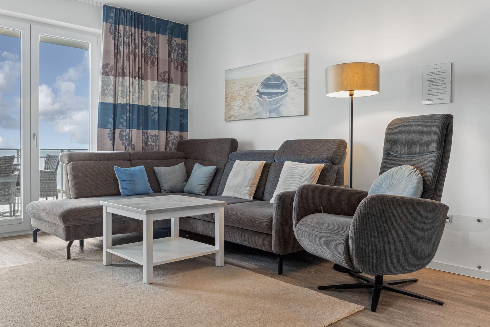 Wohnzimmer mit Sofa, Sessel und Couchtisch. Fenster mit Blick auf Balkon.