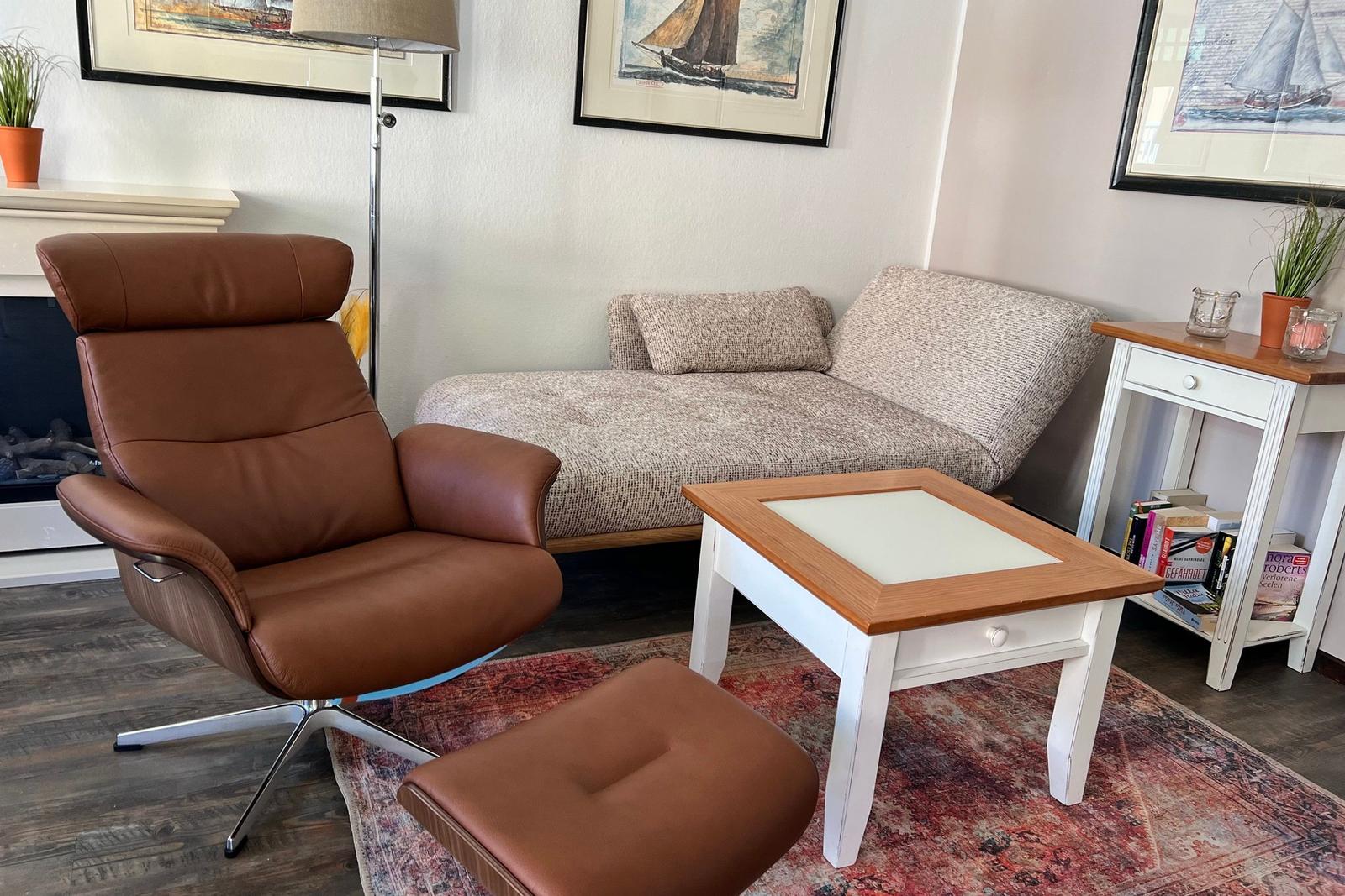 Ein Wohnzimmer mit braunem Sessel, Sofa, Tisch und Wandbildern.