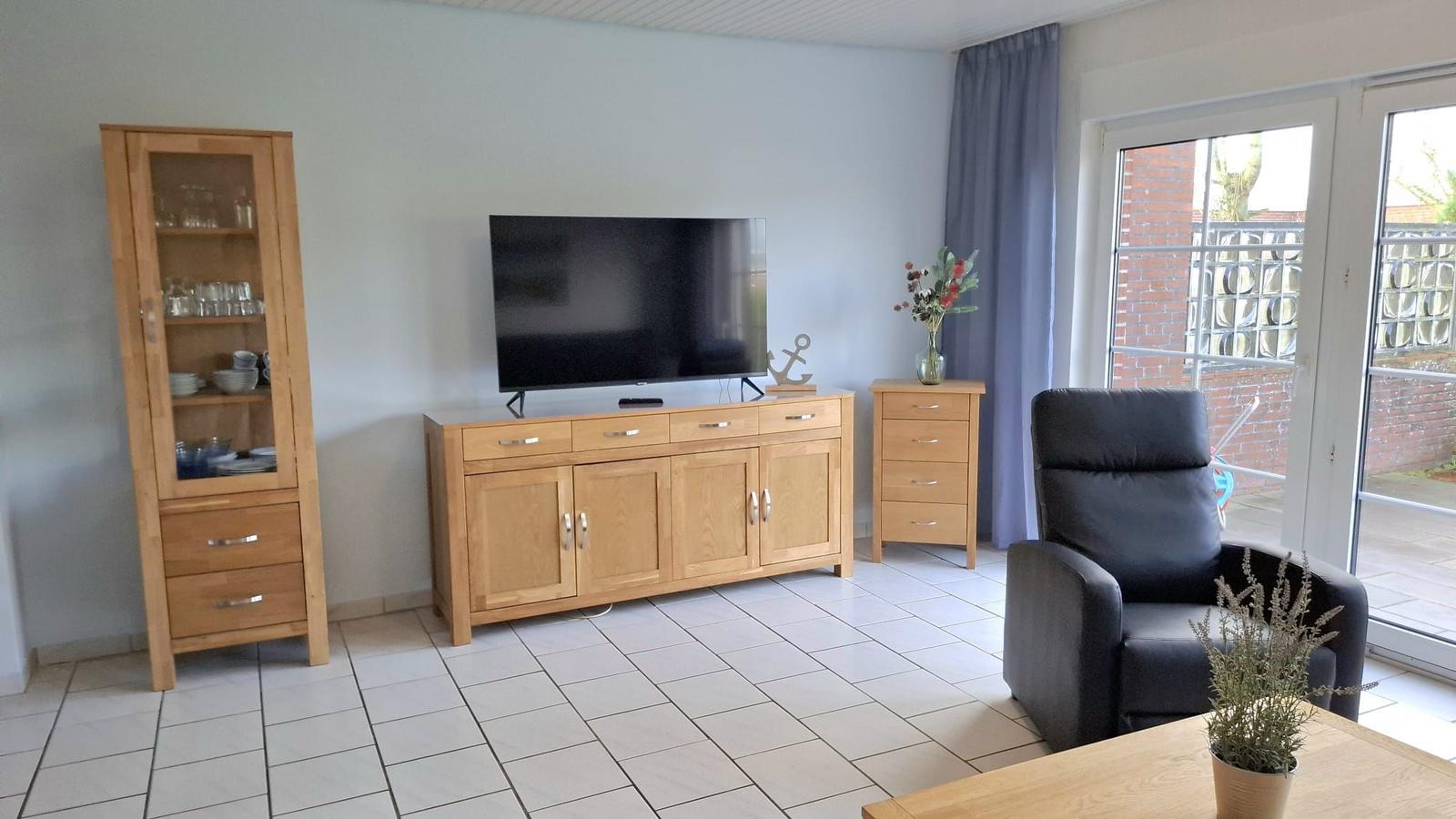Living room with TV, wooden furniture, and armchair. Access to terrace.