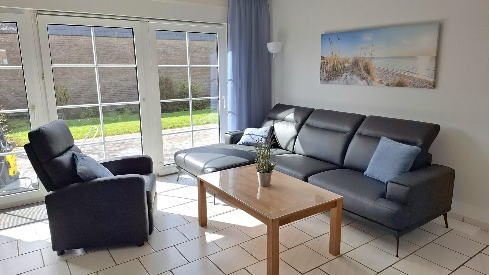 Living room with sofa, armchair, and table. Door to terrace. Wall art beach.