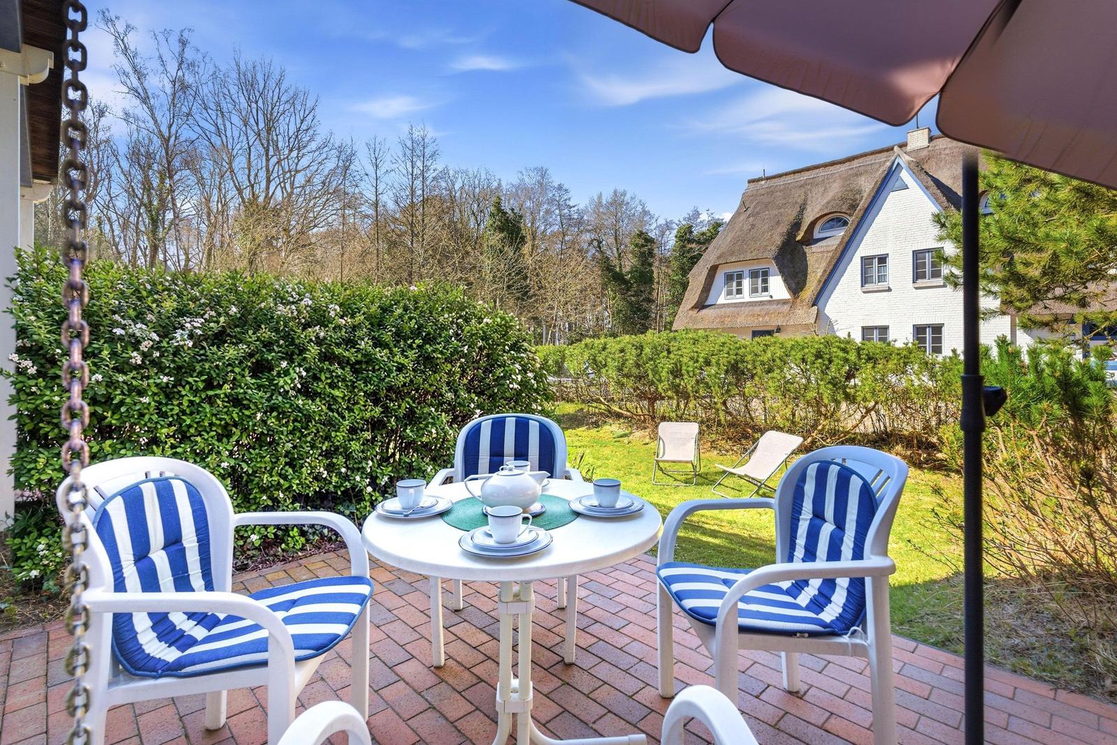 Terrasse mit Tisch, Stühlen und Sonnenschutz. Blick auf grünen Garten und traditionelles Haus.